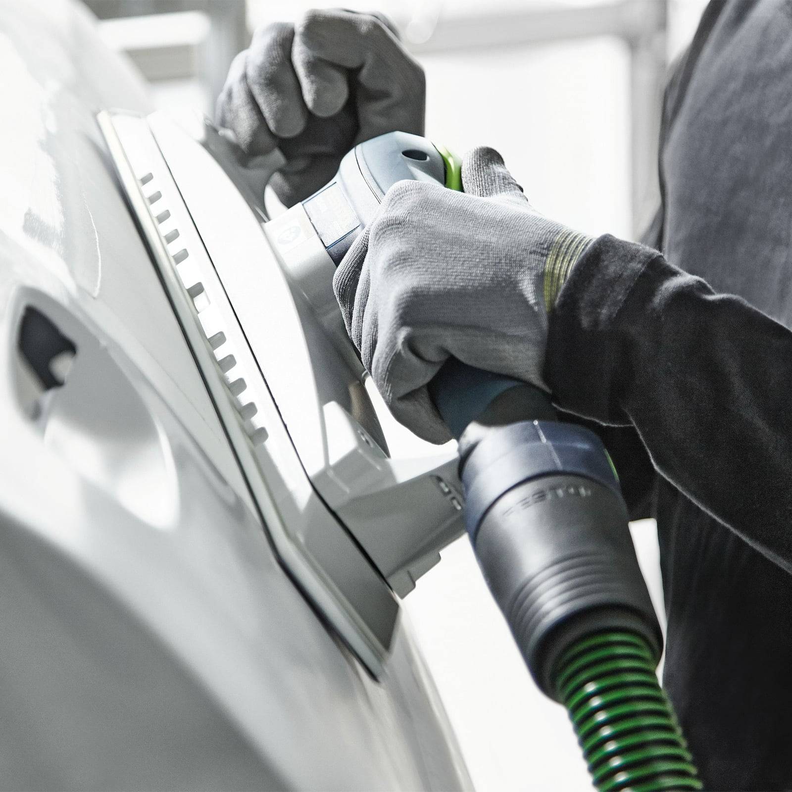 Eine Nahaufnahme der behandschuhten Hände einer Person, die eine Oberfläche mit einer elektrischen Schleifmaschine bearbeitet und dabei Präzision und Detailtreue in der Aufgabe hervorhebt.