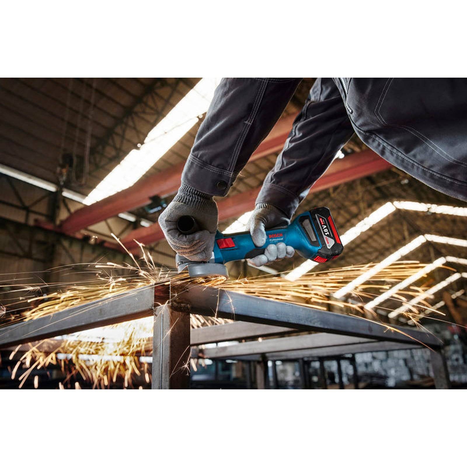 Eine Person benutzt ein Elektrowerkzeug, um einen Metallrahmen zu schleifen und erzeugt dabei helle Funken in einem großen Lagerhaus mit hoher Decke.