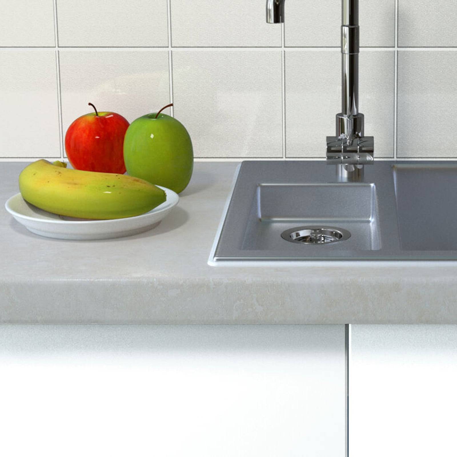 Ein Küchenwaschbecken mit einer Chromarmatur ist in eine Arbeitsplatte eingelassen. Daneben liegt auf einem Teller ein roter Apfel, ein grüner Apfel und zwei Bananen.