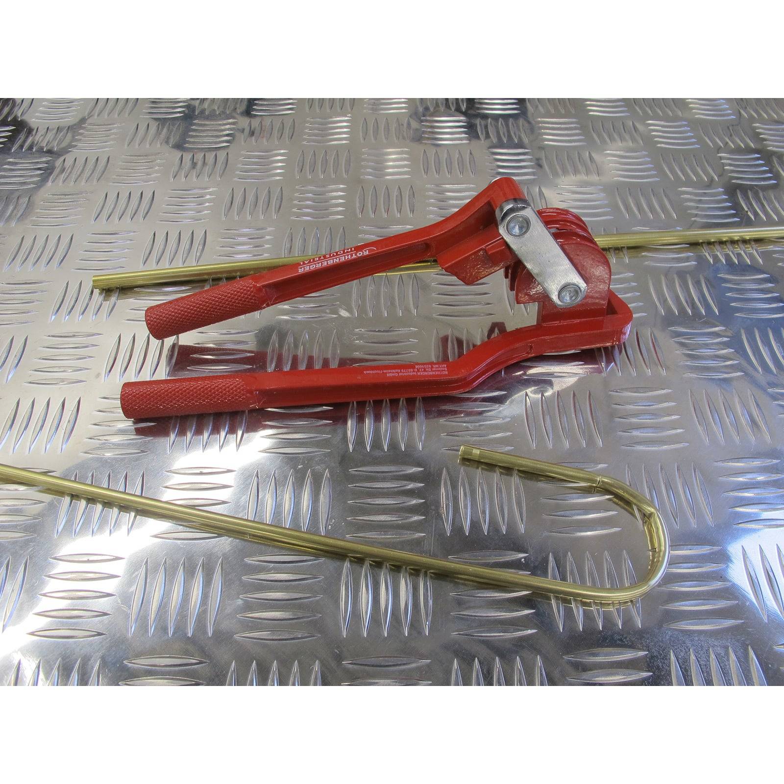 Roter Rohrbieger mit zwei gebogenen Messingröhren auf einer Metalloberfläche mit Raute.