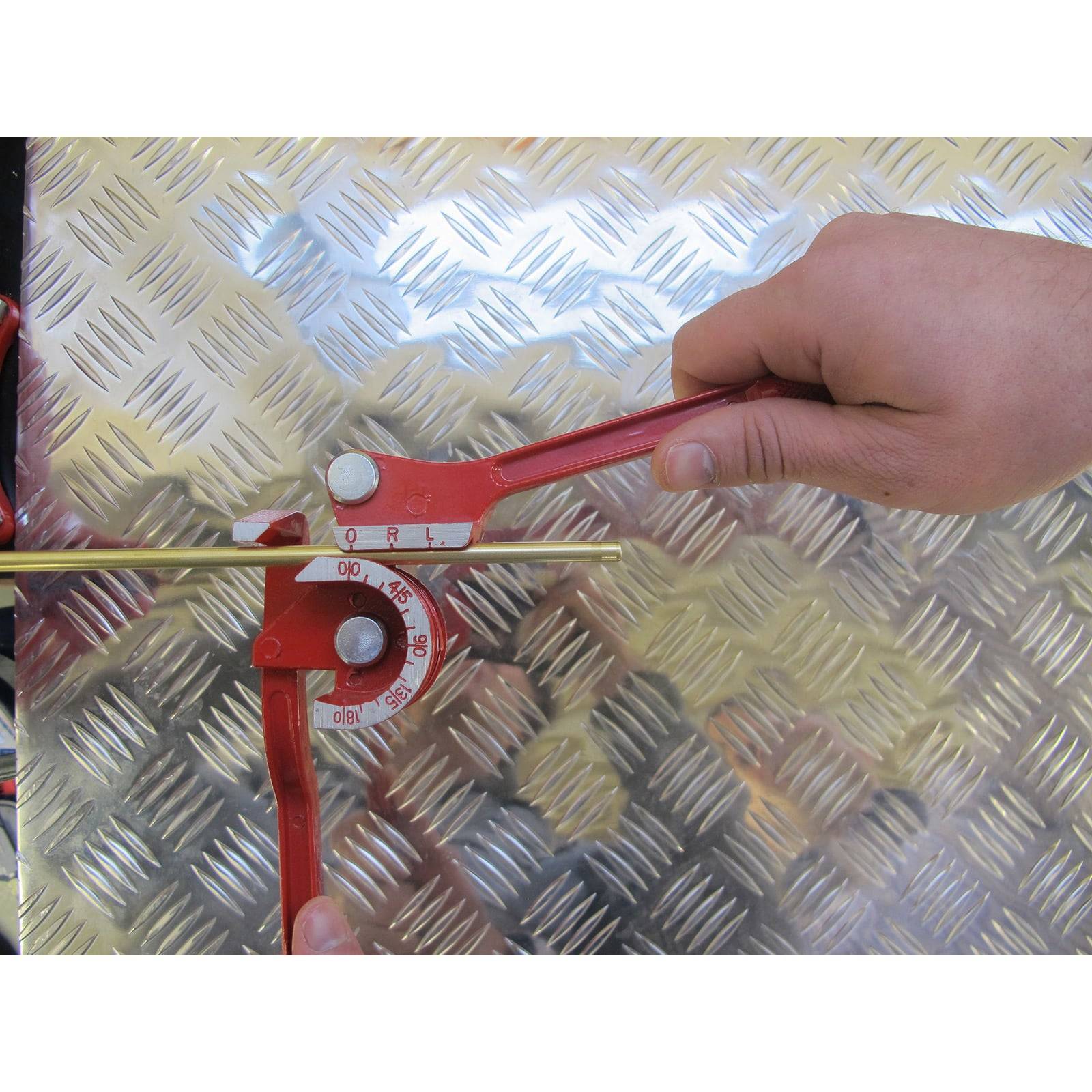 Hände, die einen roten Rohrbieger auf einer Metalloberfläche benutzen und dabei die auf dem Zifferblatt des Werkzeugs markierten Winkelmaße einstellen.