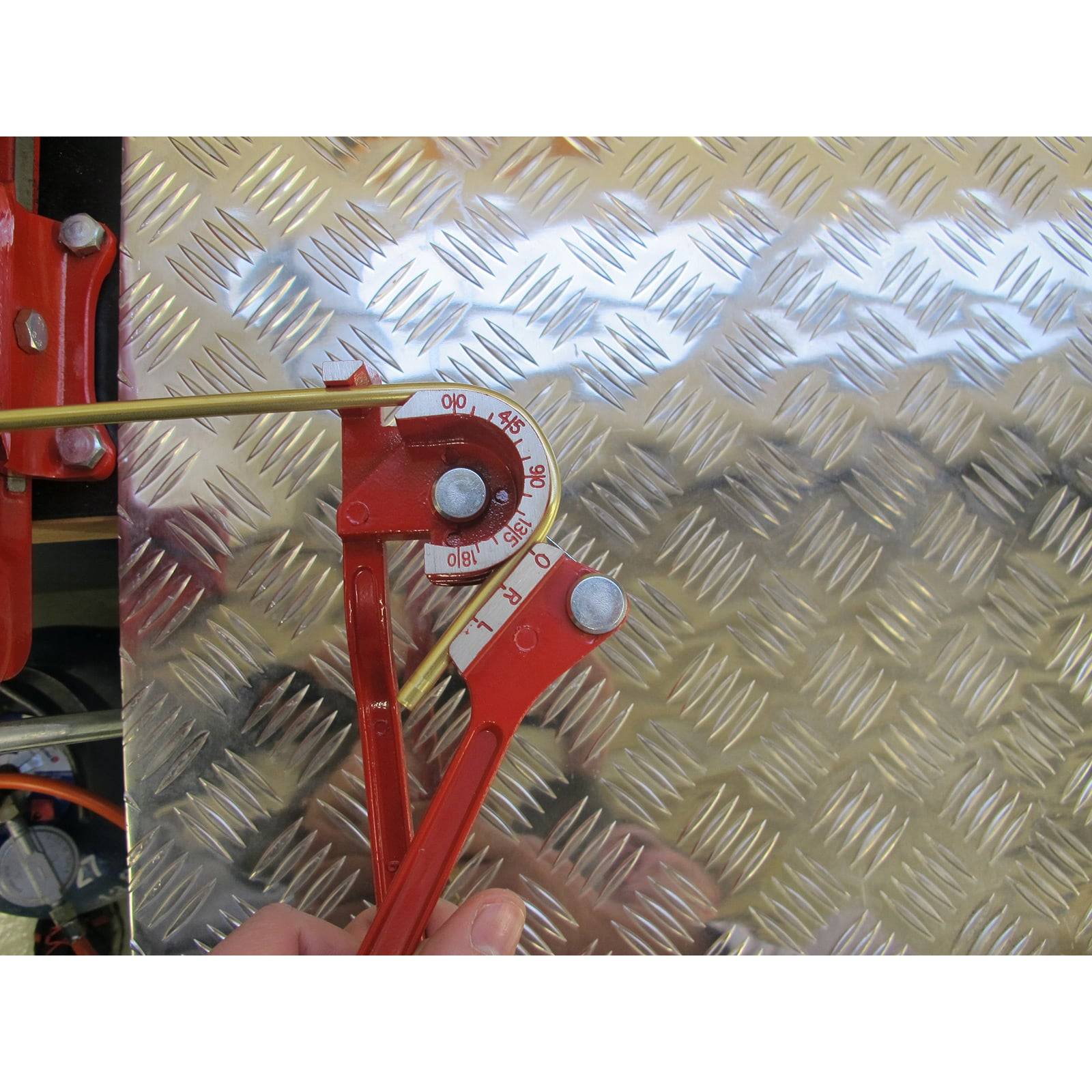 Ein rotes Metallwerkzeug, das einen Winkel gegen eine silbrig strukturierte Oberfläche misst und dabei ungefähr 45 Grad zeigt.
