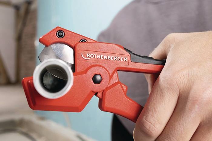 Nahaufnahme einer Hand, die einen roten Rohrbezugschneider von Rothenberger zum Schneiden eines Metallrohrs verwendet.