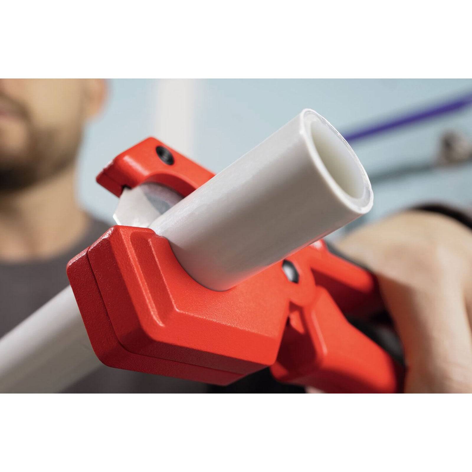 Eine Person verwendet einen roten Rohrabschneider, um ein weißes Plastikrohr zu durchtrennen und führt damit eine Klempneraufgabe vor.