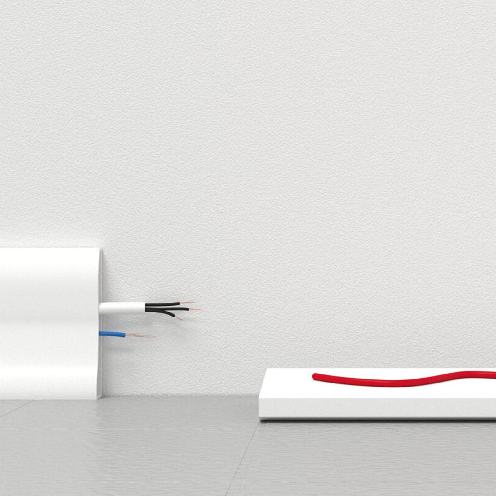 Eine weiße Wand und ein weißer Boden mit rotem Kabel auf einer weißen Oberfläche; blaue und schwarze Kabel ragen aus einer weißen Box auf dem Boden.