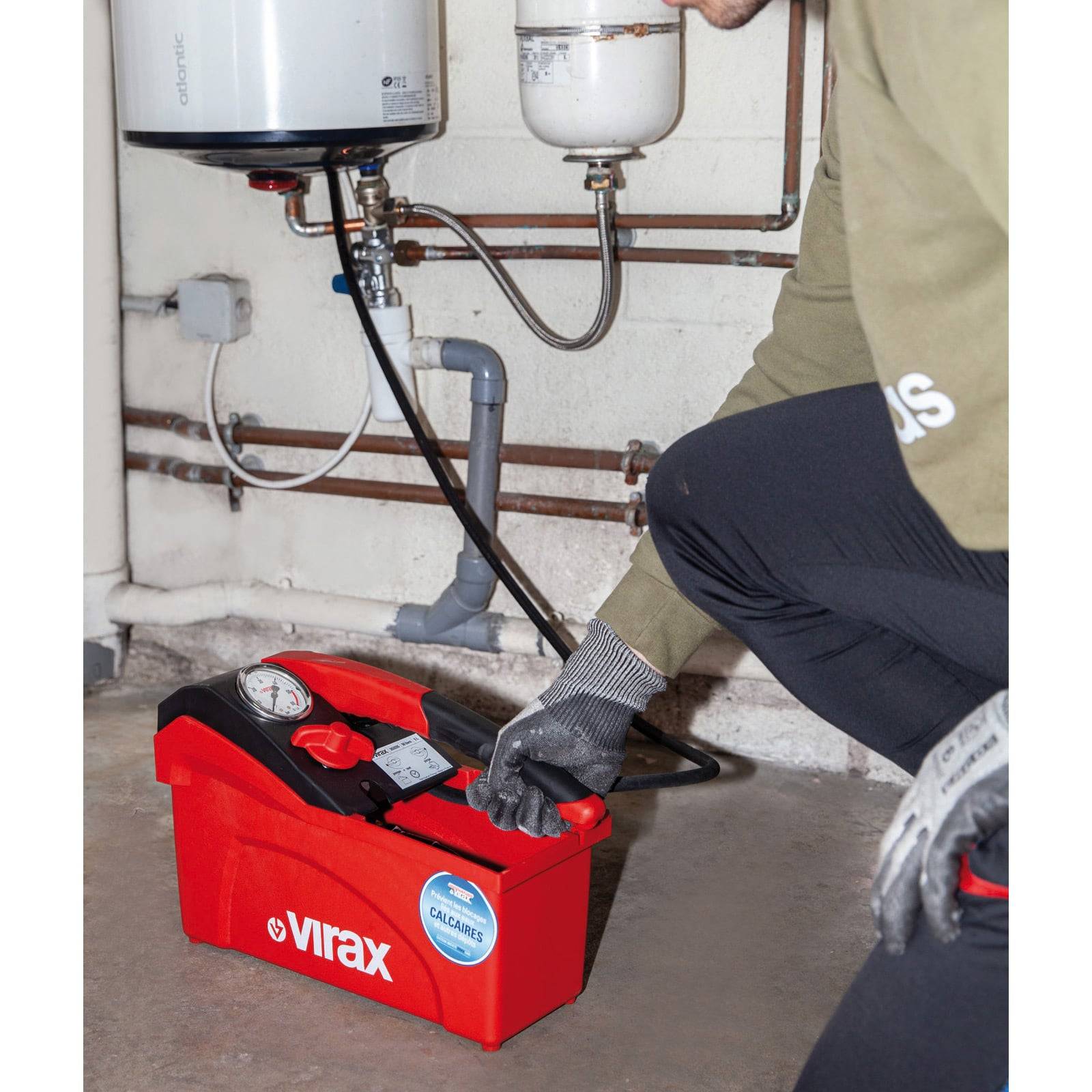 Person mit einer roten Virax-Druckprüfpumpe, die an Sanitärrohre angeschlossen ist und Lecks in einer Wohnumgebung überprüft.