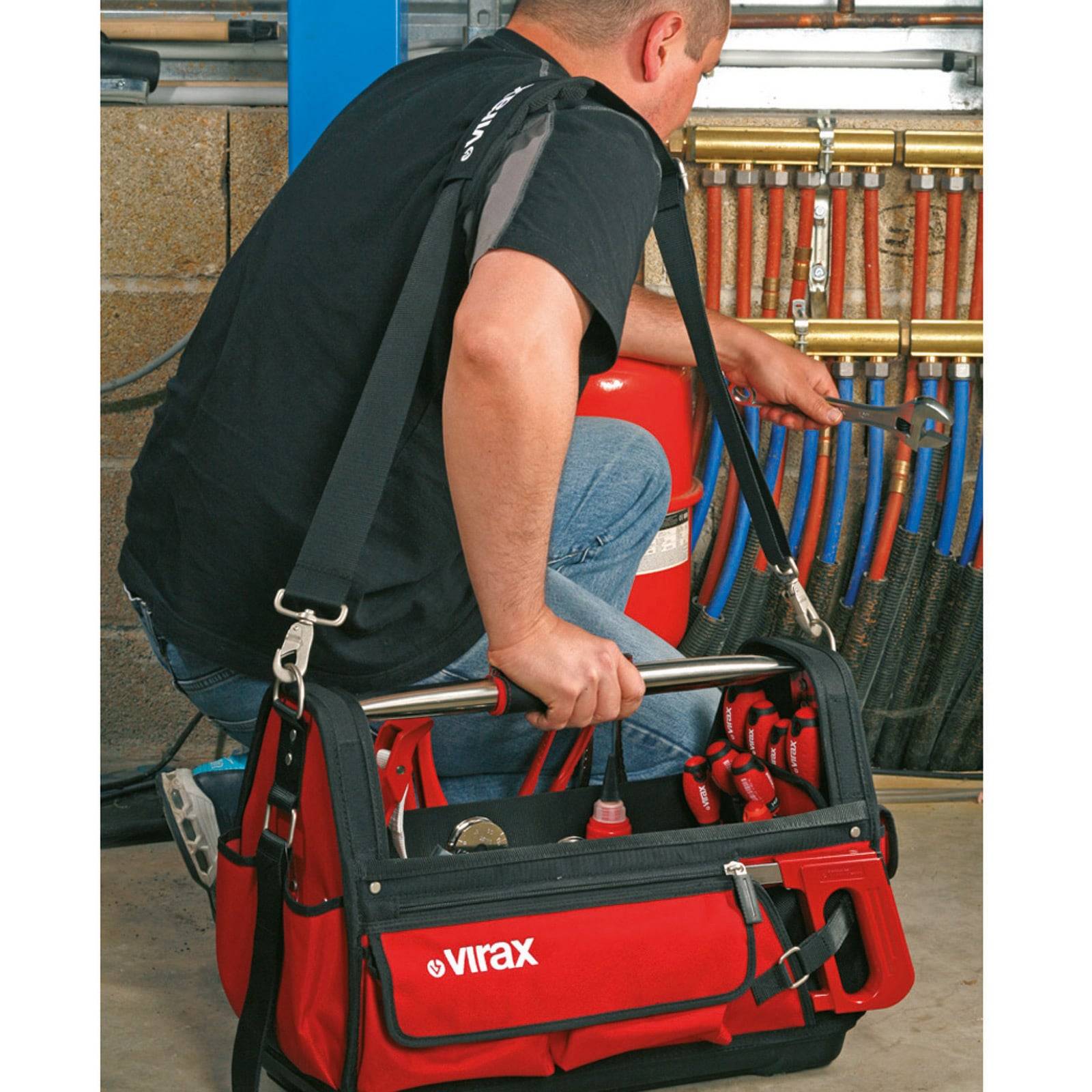 Eine Person, die Werkzeuge aus einer roten Virax-Werkzeugtasche verwendet, um Ventile an Metallrohren einzustellen, was auf Sanitär- oder Wartungsarbeiten hindeutet.