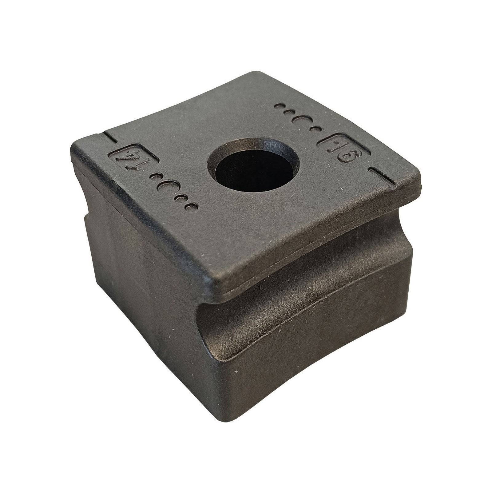 Ein quadratisches, graues mechanisches Teil mit einem zentralen Loch und gravierten Symbolen oben. Es scheint eine Befestigungs- oder Stützkomponente zu sein.