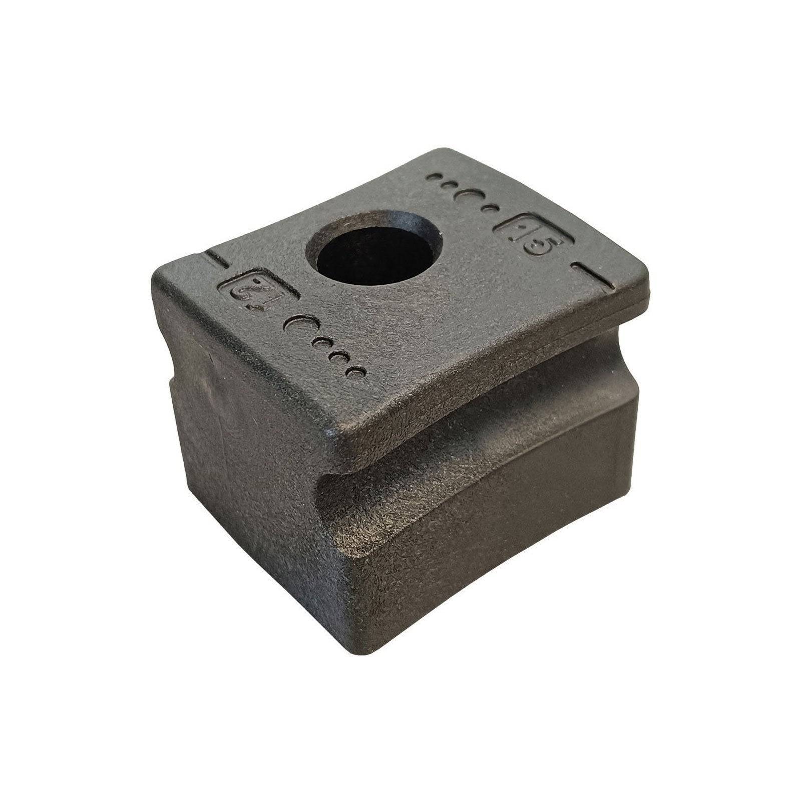 Ein quadratischer schwarzer Block mit einem zentralen kreisförmigen Loch und eingravierter Symbolik auf der Oberfläche, wahrscheinlich als Gewicht oder für Konstruktionszwecke verwendet.