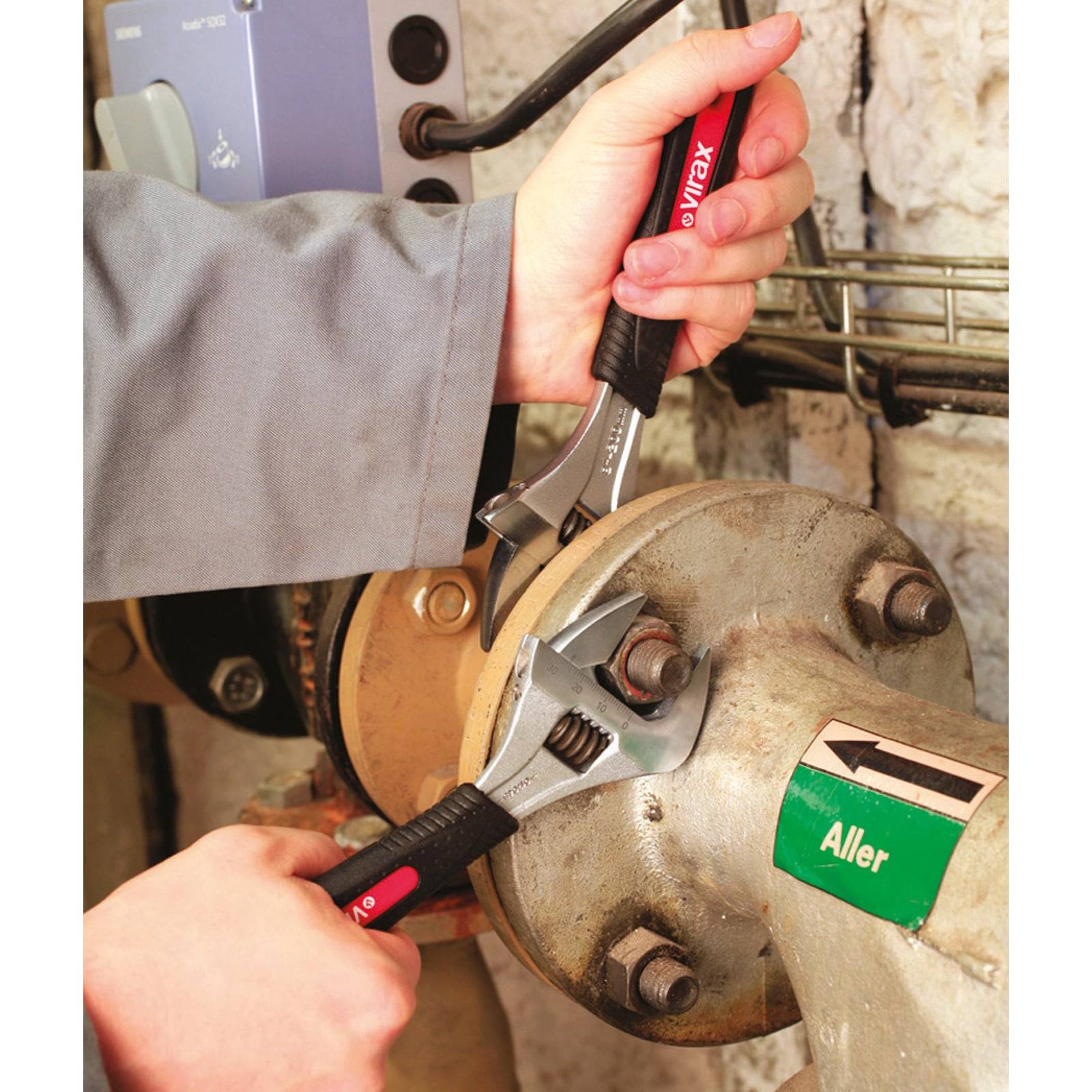 Eine Person verwendet zwei einstellbare Schraubenschlüssel, um Bolzen an industriellen Rohrleitungen anzuziehen, wobei eine grüne 