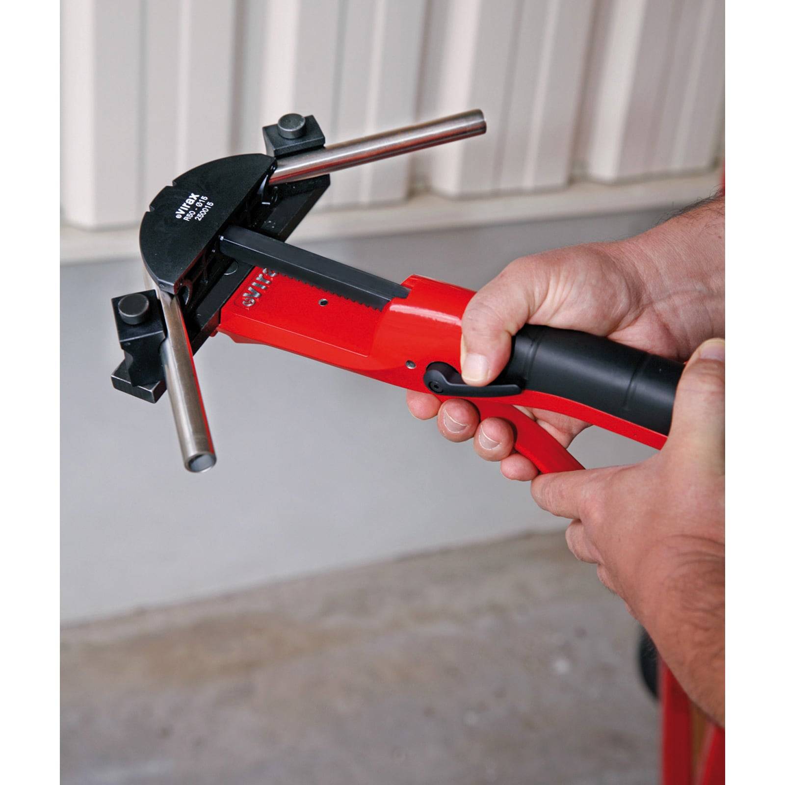 Hände, die ein rotes manuelles Heftwerkzeug gegen eine gewellte Oberfläche verwenden und dabei einen Installationsprozess demonstrieren.