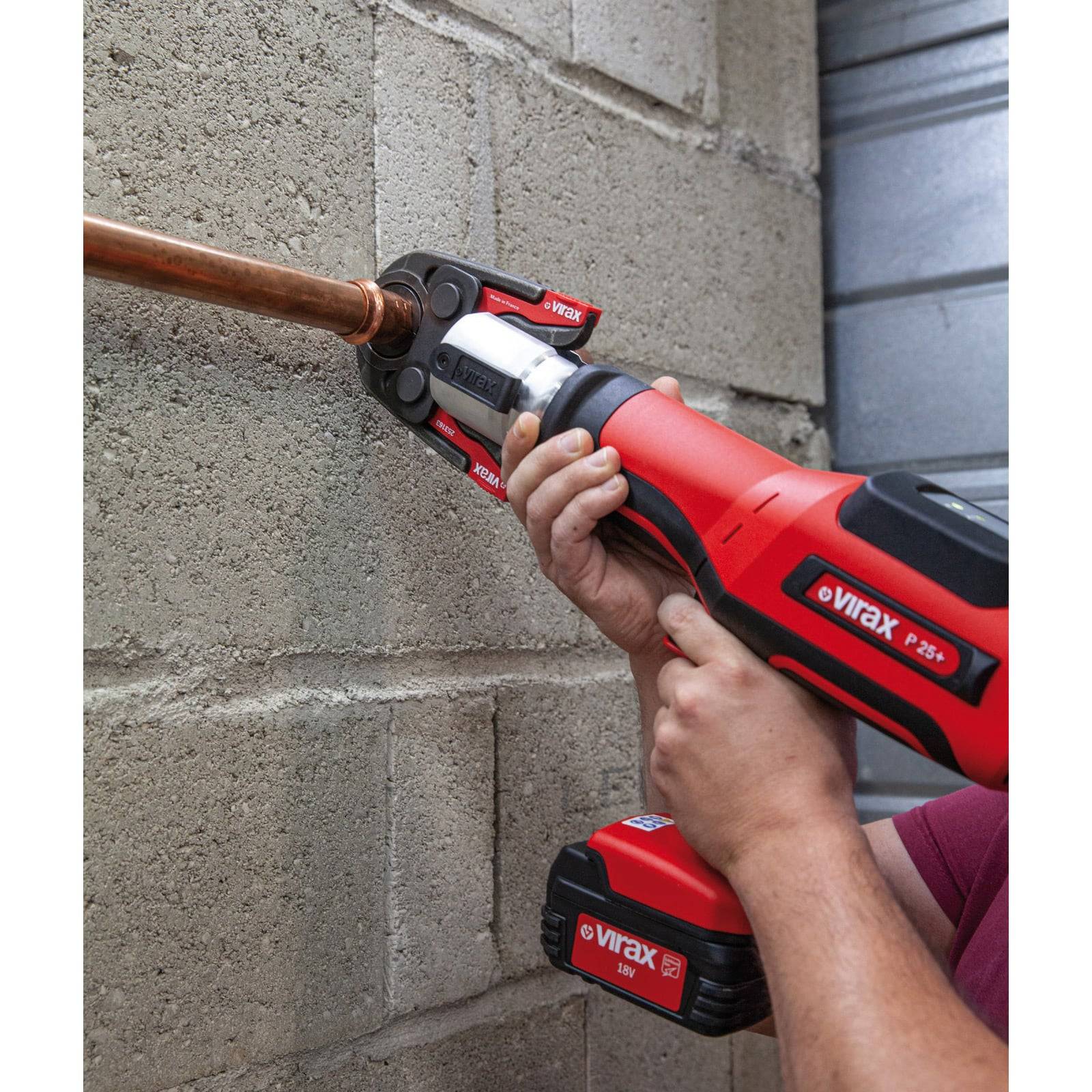 Eine Person verwendet ein rotes Virax-Presswerkzeug, um ein Kupferrohr mit einer Wandarmatur zu verbinden, was auf laufende Klempner- oder Wartungsarbeiten hinweist.