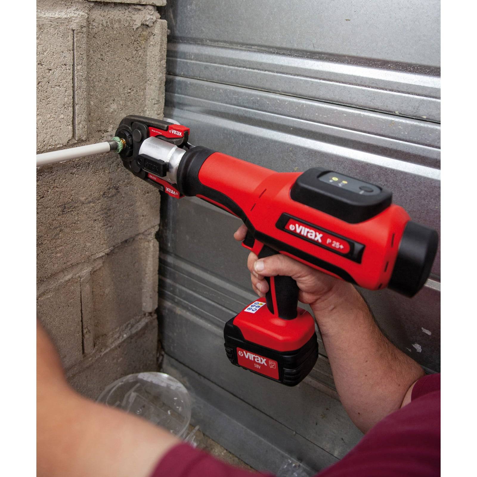 Eine Person verwendet ein rotes elektrisches Werkzeug, um an einem Rohr vor einer Betonwand zu arbeiten und demonstriert dabei dessen Anwendung bei der Rohrinstandhaltung.