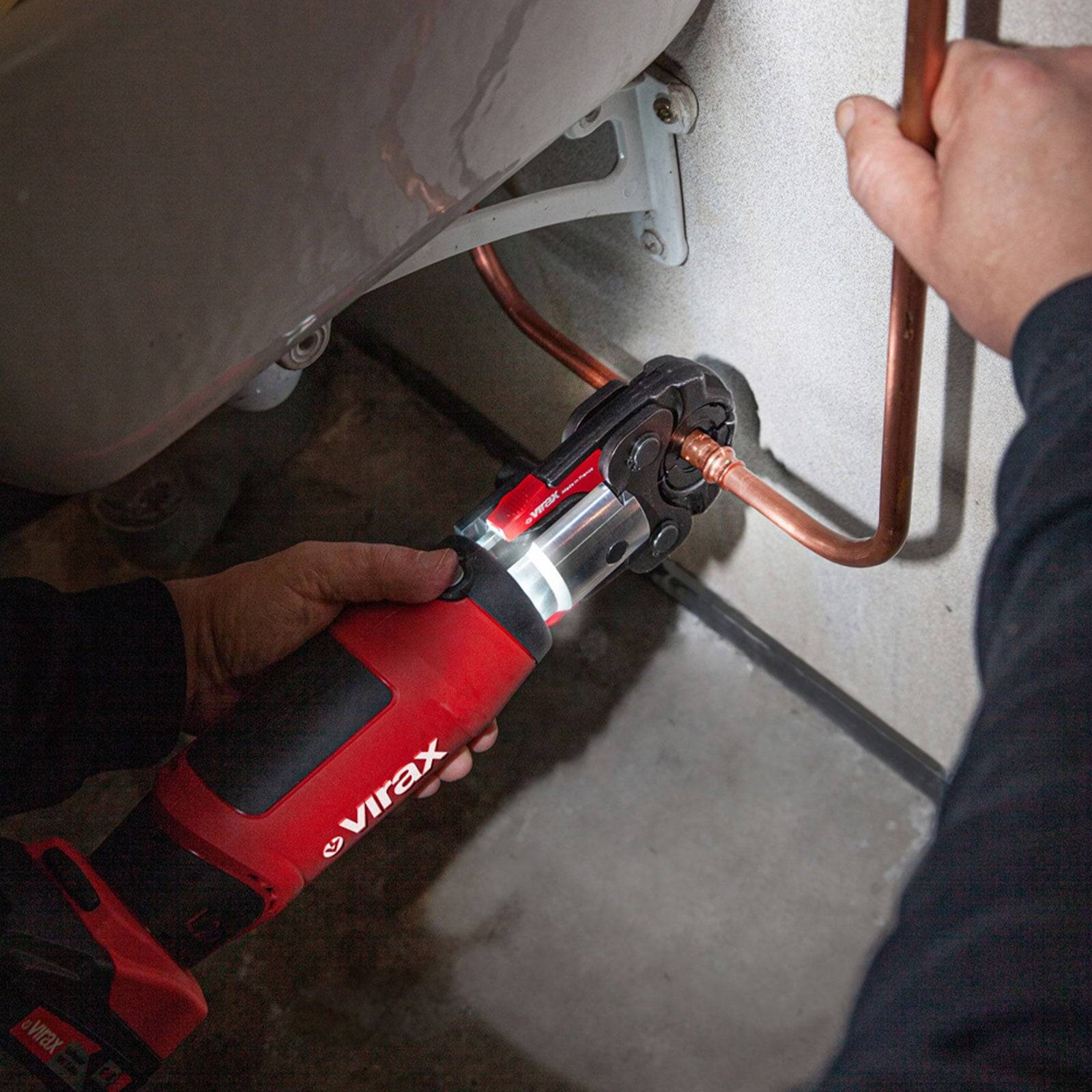 Eine Person benutzt ein rotes Elektrowerkzeug, um ein Kupferrohr an einer Wand zu befestigen. Das Werkzeug wird in einer Hand gehalten, wobei eine Nahaufnahme der Aktion zu sehen ist.