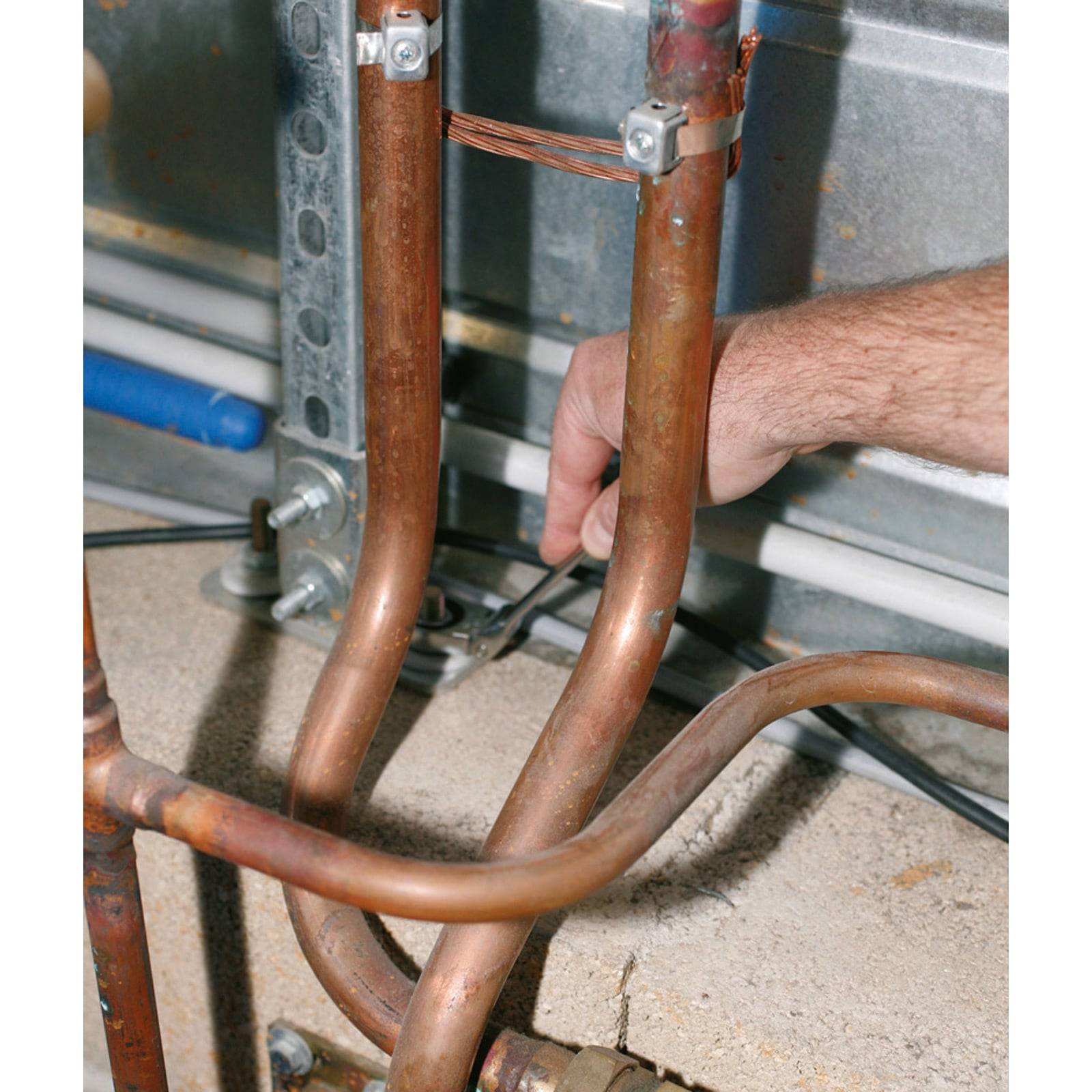 Eine Person passt Kupferrohre mit einem Schraubenschlüssel an. Die Rohre sind Teil eines Installationssystems, mit sichtbaren Verbindungsstücken und Drähten im Hintergrund.
