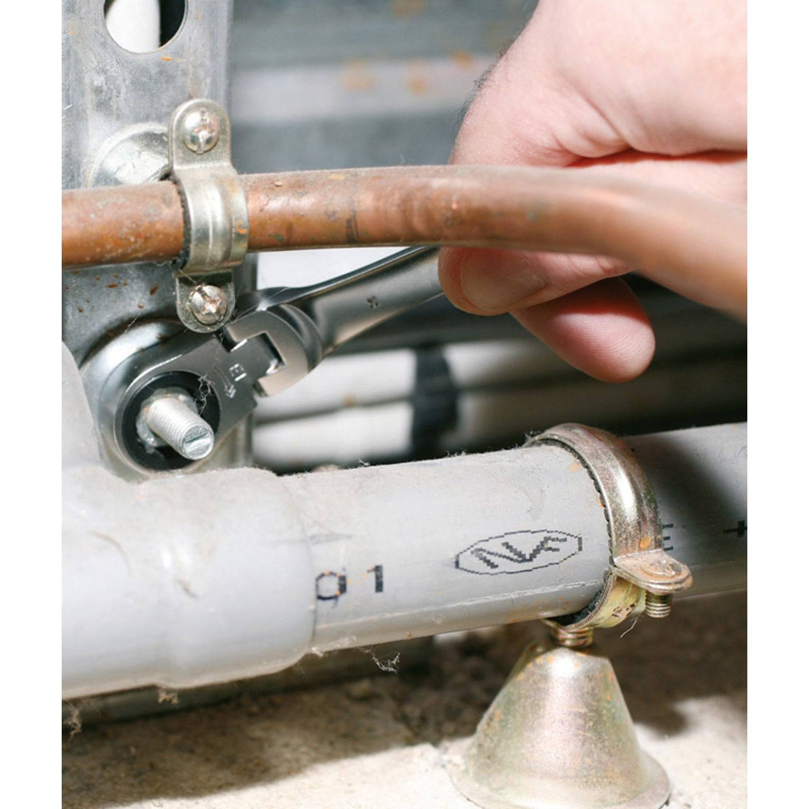 Eine Hand, die einen Schraubenschlüssel benutzt, um einen Metallrohranschluss in der Nähe anderer Rohre festzuziehen.