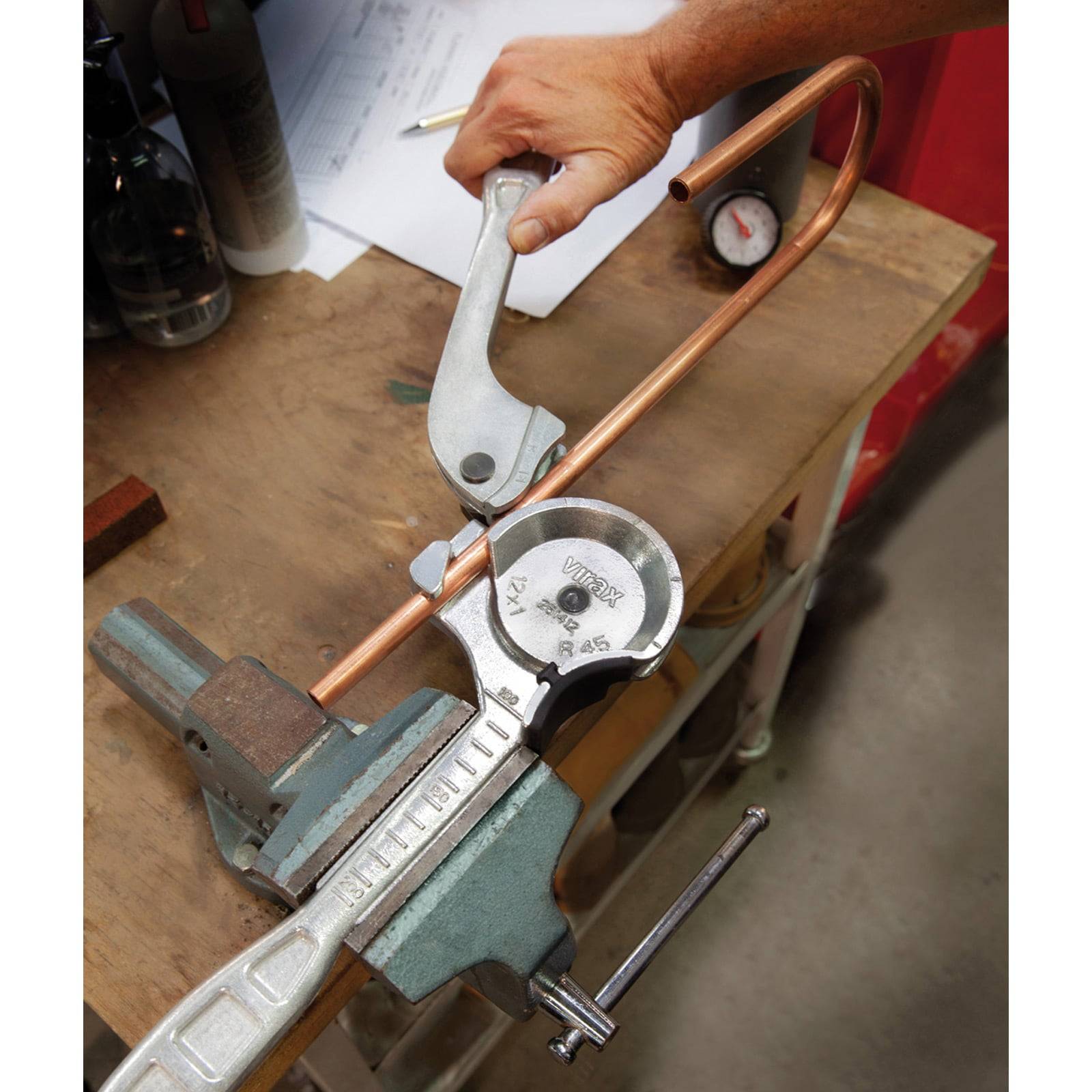 Eine Person benutzt einen manuellen Rohrbieger, um ein Kupferrohr auf einer Werkbank zu formen, was auf eine handwerkliche Tätigkeit oder laufende Klempnerarbeit hinweist.