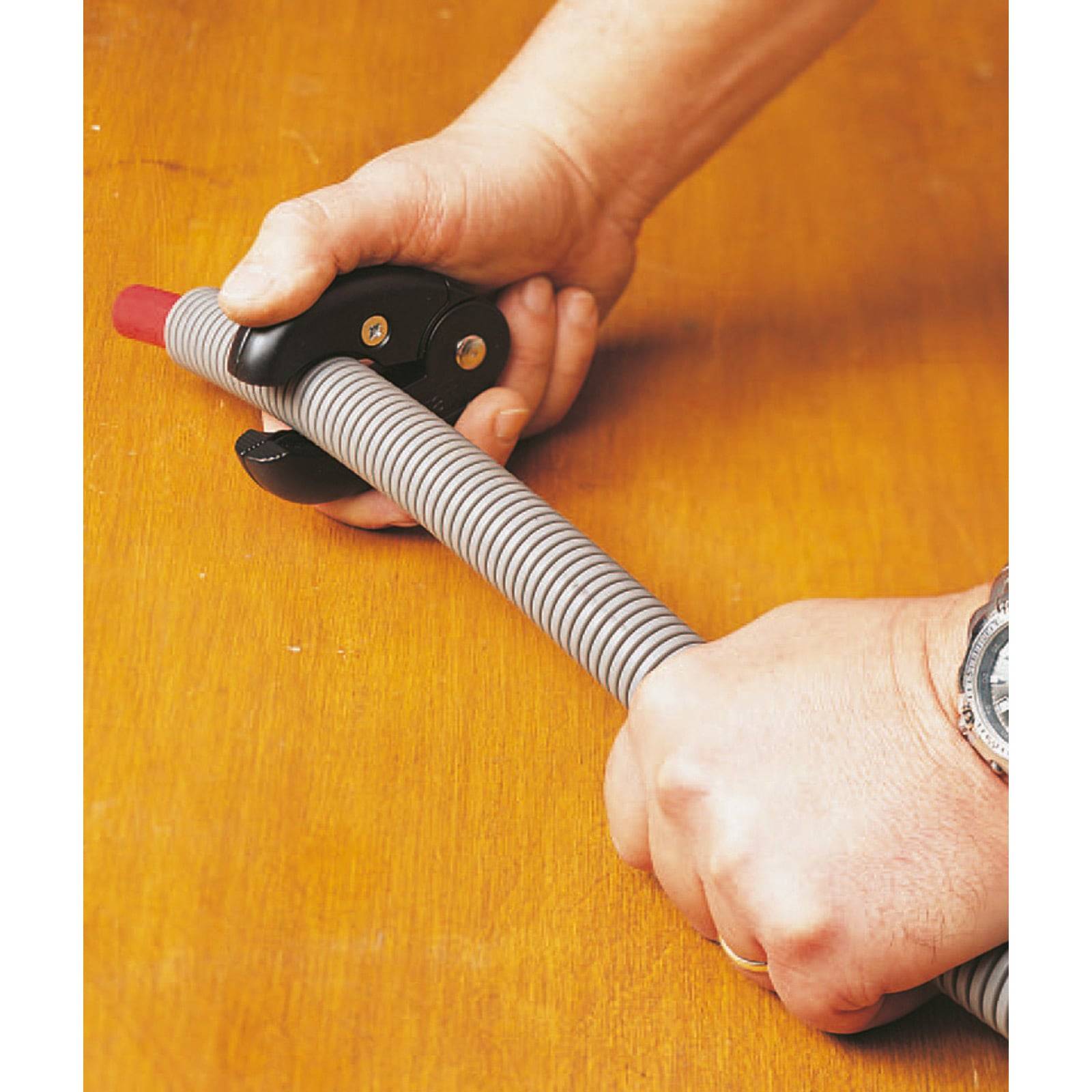 Zwei Hände demonstrieren, wie man ein Werkzeug mit einem langen, spiralförmigen Griff und einer roten Spitze auf einer Holzoberfläche greift.