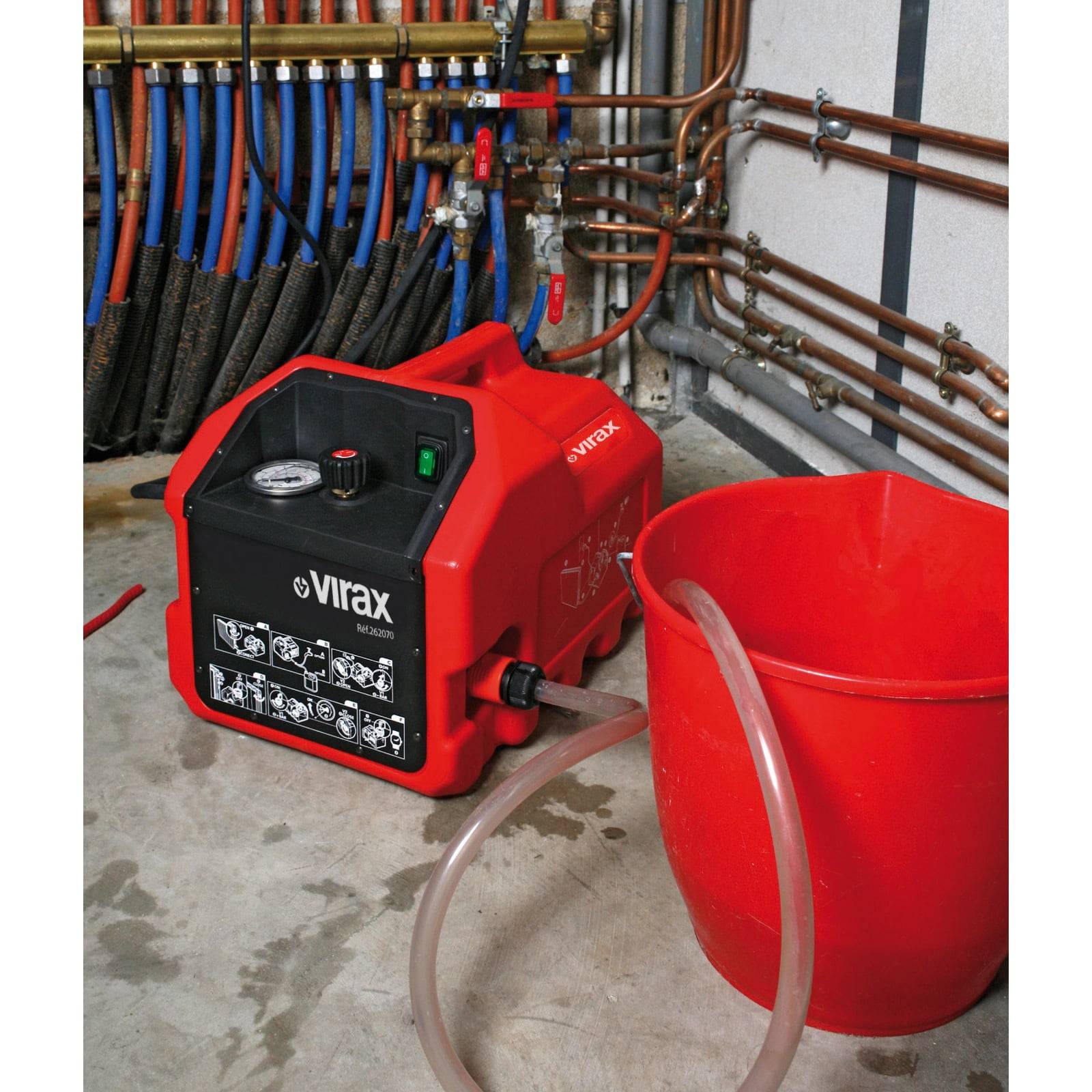 Eine rote Rohrreinigungsmaschine, die an Sanitärrohre angeschlossen ist, mit einem roten Eimer in der Nähe, die zum Reinigen und Warten von Heizungssystemen verwendet wird.