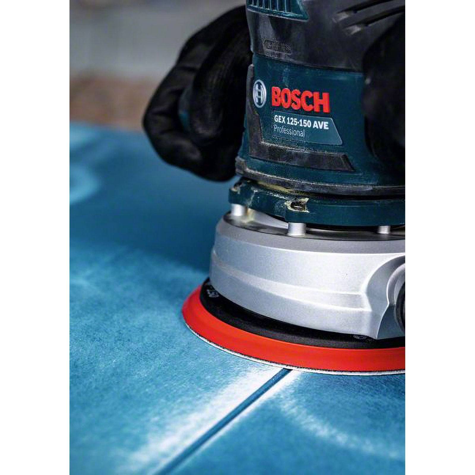 Eine Hand hält einen Bosch GEX 125-150 AVE Professional Schleifer und glättet eine blaue Oberfläche, was auf eine Holzbearbeitung oder Oberflächenbehandlungsaufgabe hindeutet.