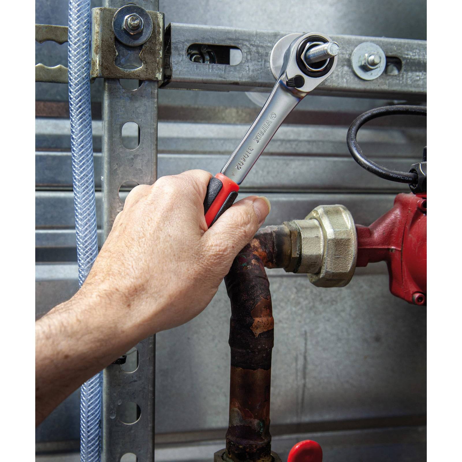 Eine Hand benutzt einen Schraubenschlüssel, um einen Bolzen an einem Metallrohr zu befestigen, der Teil einer industriellen Maschine ist. Die Umgebung scheint ein Wartungsbereich zu sein.