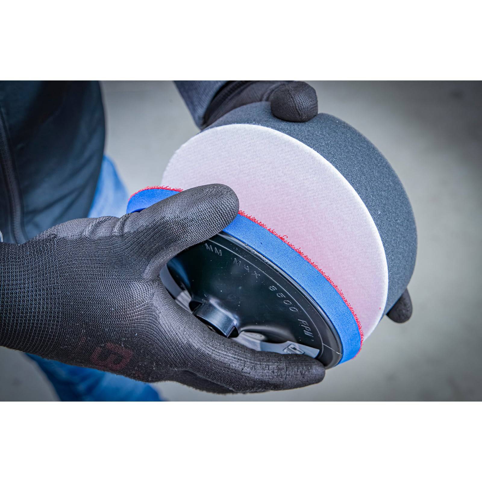 Eine Person trägt schwarze Handschuhe und hält ein rundes, schwarz-weißes Schleifwerkzeug, was Sicherheit und Präzision bei DIY-Aufgaben unterstreicht.