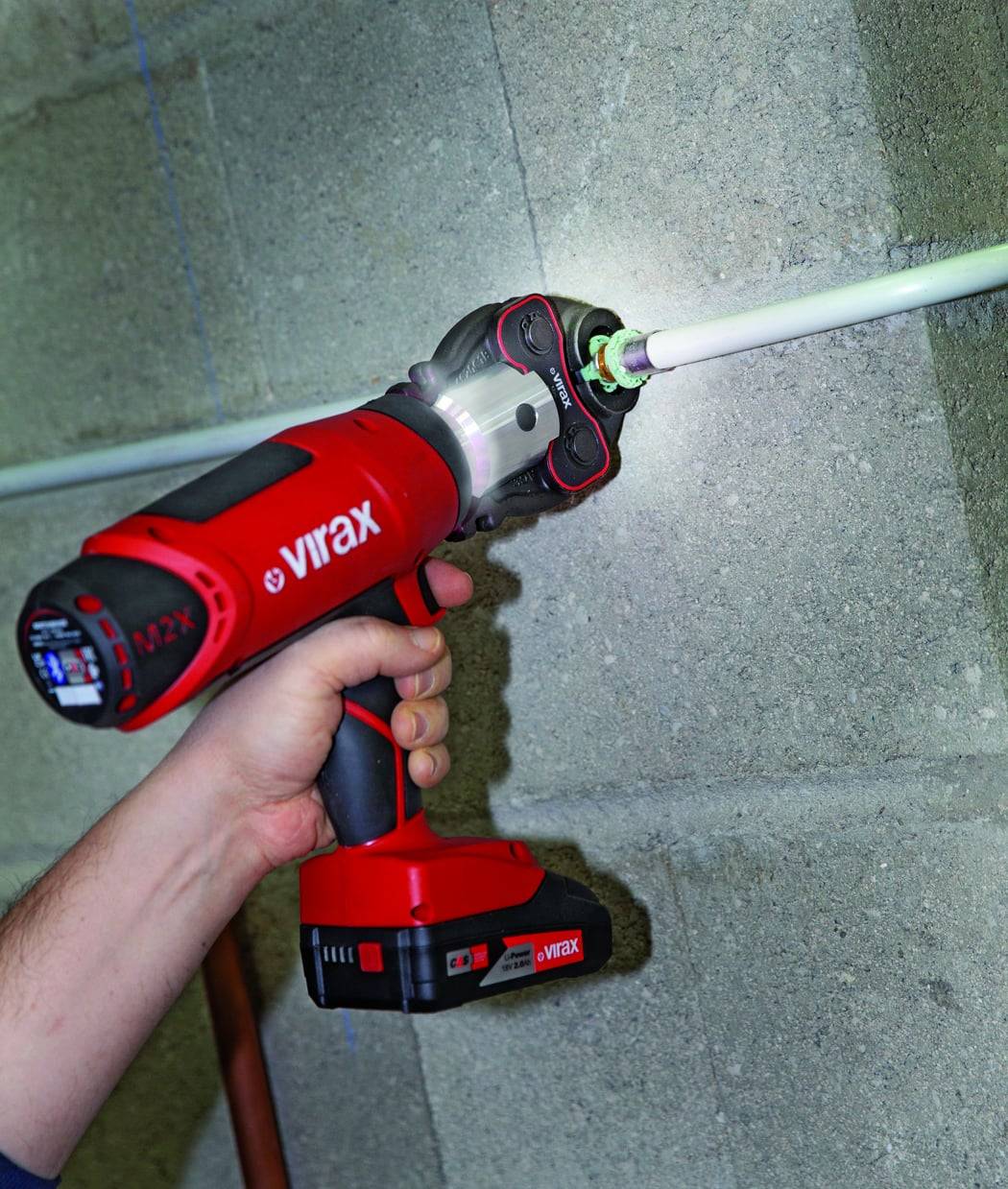 Person, der ein rotes Virax-Elektrowerkzeug verwendet, um eine Fitting an einem Metallrohr gegen eine Betonwand zu befestigen.