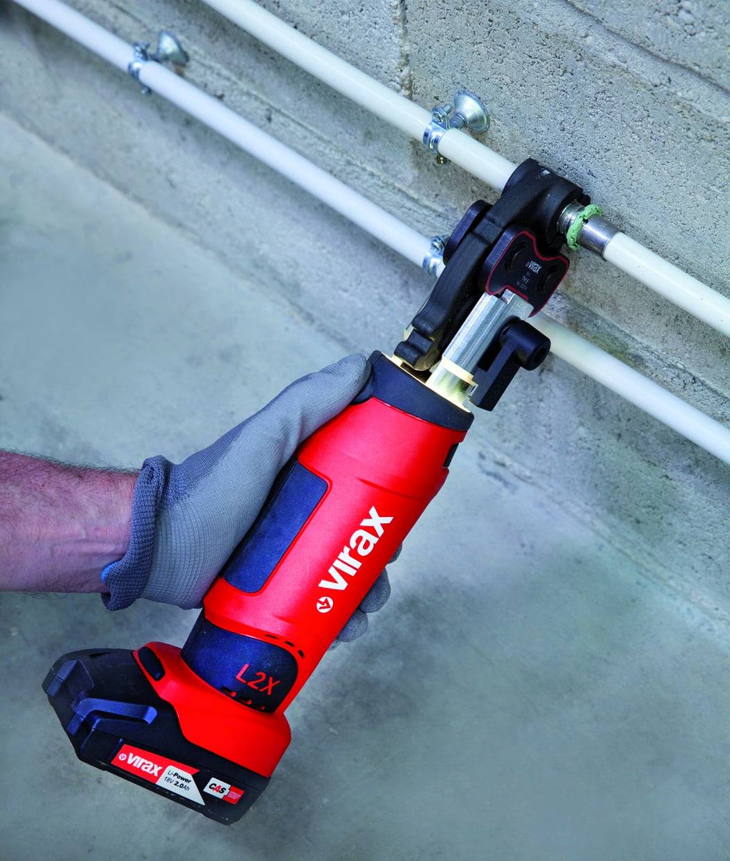 Eine Person mit einem grauen Handschuh verwendet ein rotes Viarx L2X-Werkzeug, um an einem Rohr zu arbeiten, das an einer Betonwand befestigt ist. Das Werkzeug wird in der rechten Hand gehalten.