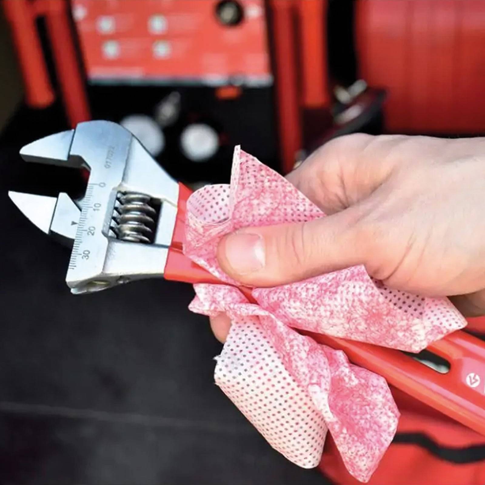 Eine Hand hält einen roten verstellbaren Schraubenschlüssel, der mit einem rosa Tuch gereinigt wird, vor einem Hintergrund von roter und schwarzer Werkzeugaufbewahrung.