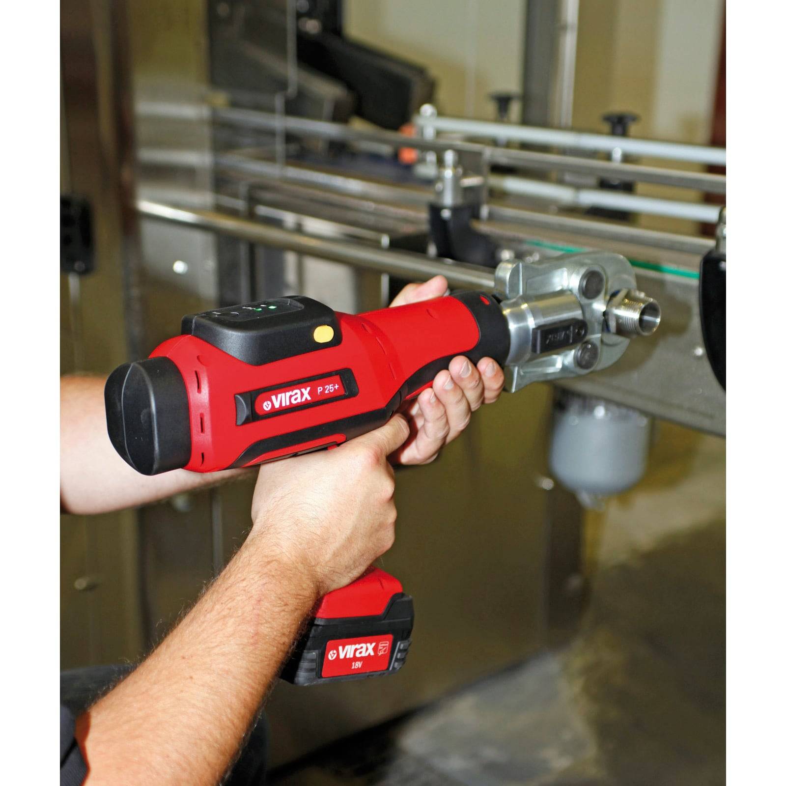 Eine Person verwendet ein rotes Virax P25+ Werkzeug, um Rohre in einer industriellen Umgebung anzupassen und demonstriert dabei die Funktionalität und ergonomische Gestaltung des Werkzeugs.