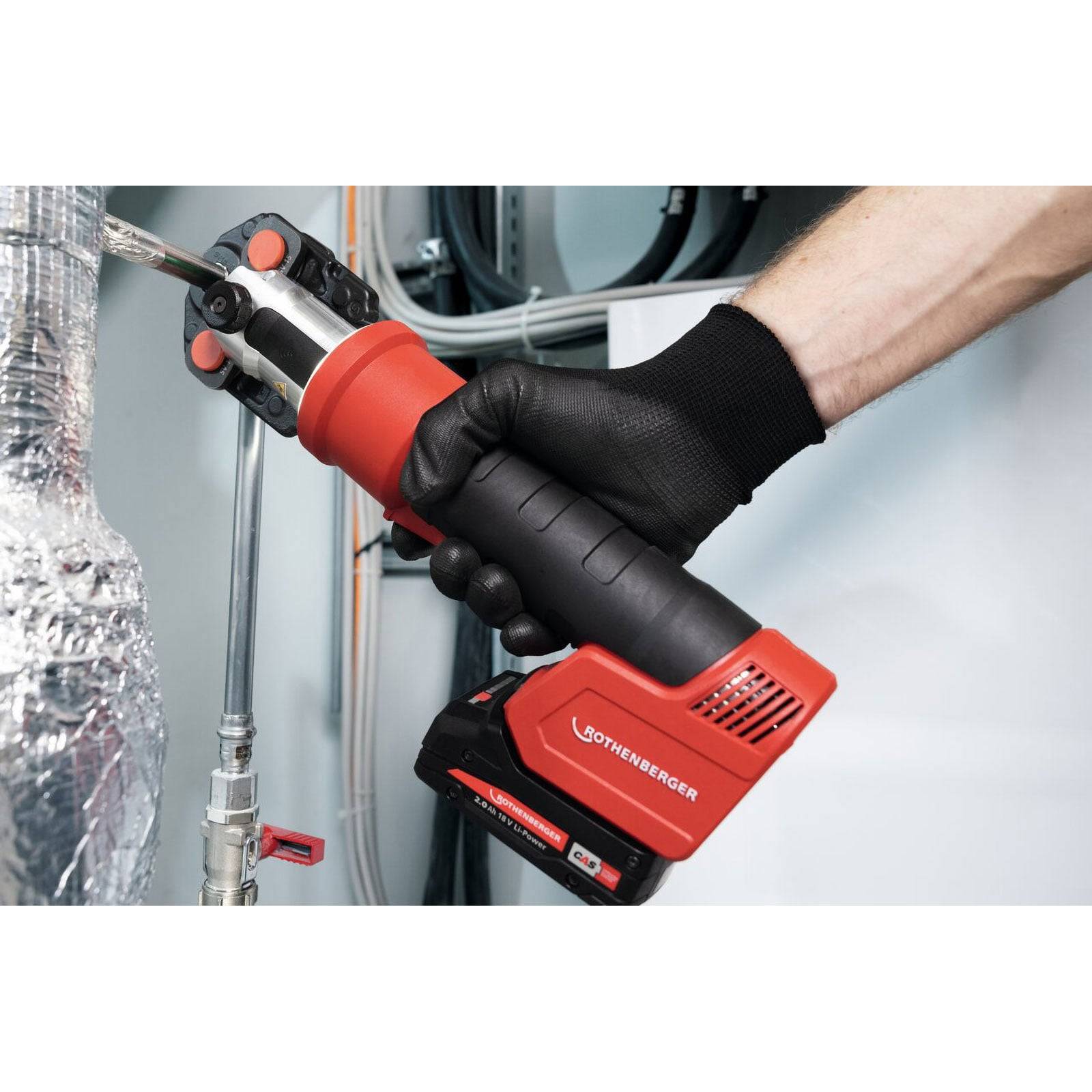 Eine Person, die ein rotes Elektrowerkzeug verwendet, um ein Metallrohr in einer mechanischen oder industriellen Umgebung zu klemmen oder zu schneiden.