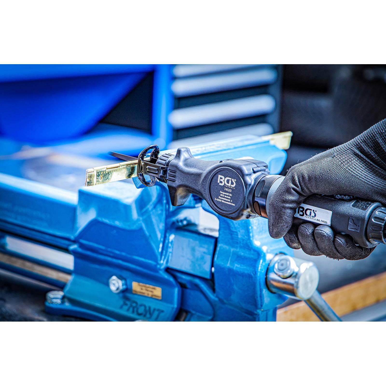 Eine Person mit Handschuhen benutzt einen blauen Schraubstock und ein Werkzeug, um ein Metallobjekt zu schneiden, was auf eine Werkstatt- oder Fertigungsumgebung hindeutet.