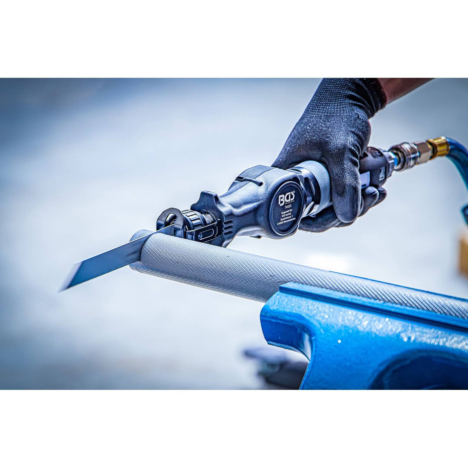 Eine Person mit Handschuhen verwendet ein pneumatisches Werkzeug, um ein zylindrisches Objekt in einer Werkstattumgebung zu schneiden oder zu formen.