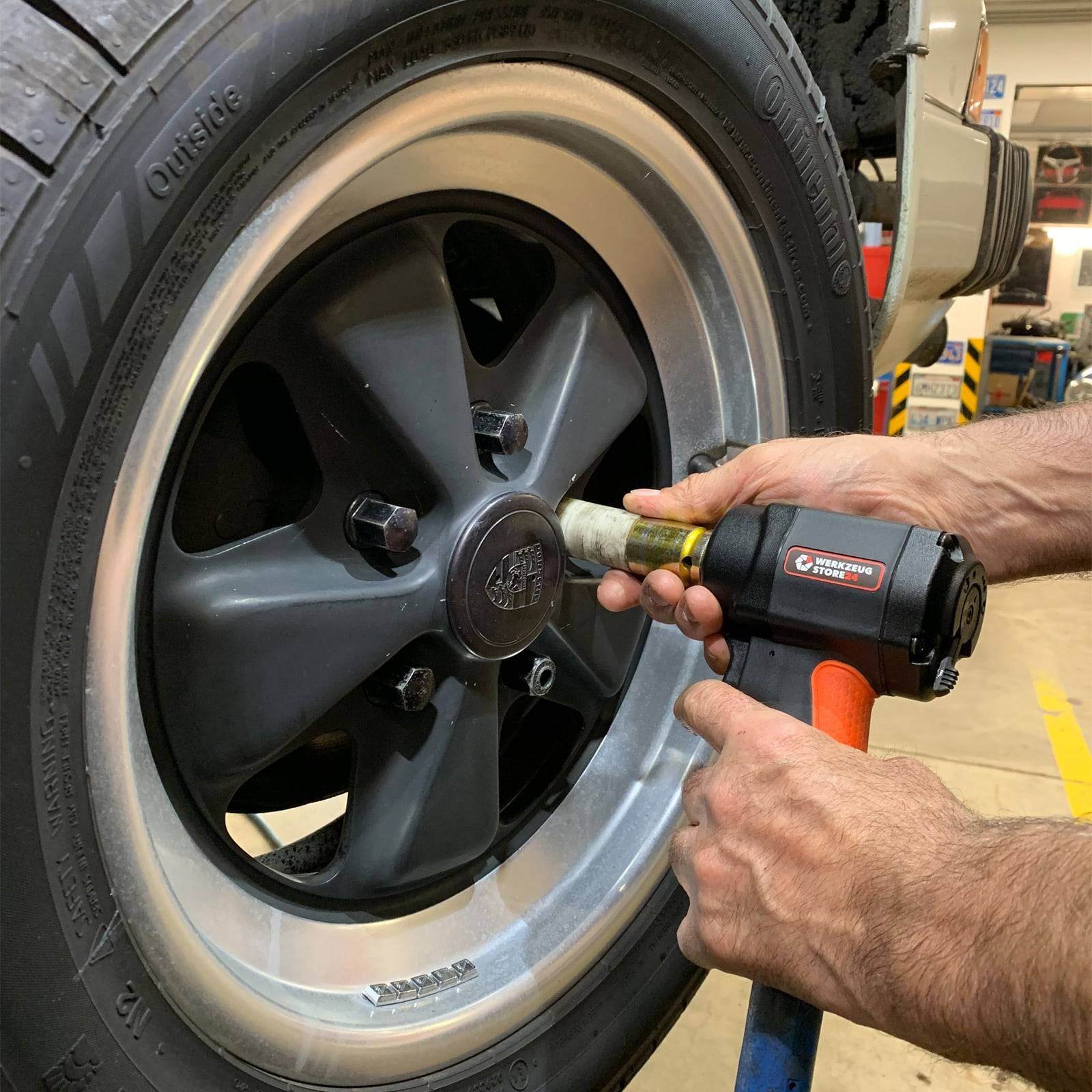 Eine Person verwendet eine Schlagschrauber, um eine Radmutter an einem Autoreifen zu festigen, wobei der Fokus auf der Anwendung des Werkzeugs in einer Werkstattsumgebung liegt.