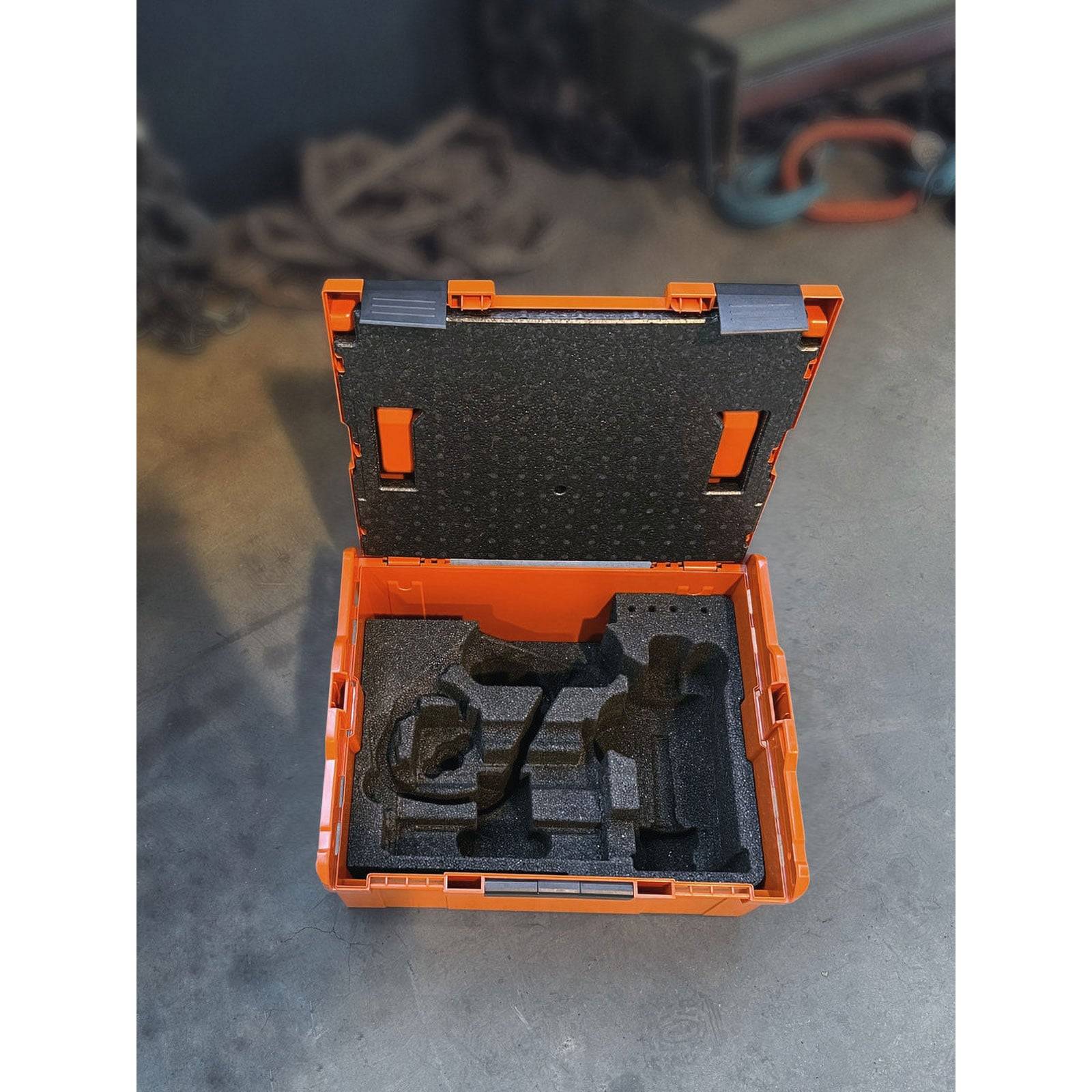 Eine orangefarbene Werkzeugkiste, die auf einem Betonboden geöffnet ist und Schaumstoffausschnitte offenbart, die darauf ausgelegt sind, verschiedene Werkzeuge und Ausrüstungsgegenstände sicher zu halten.