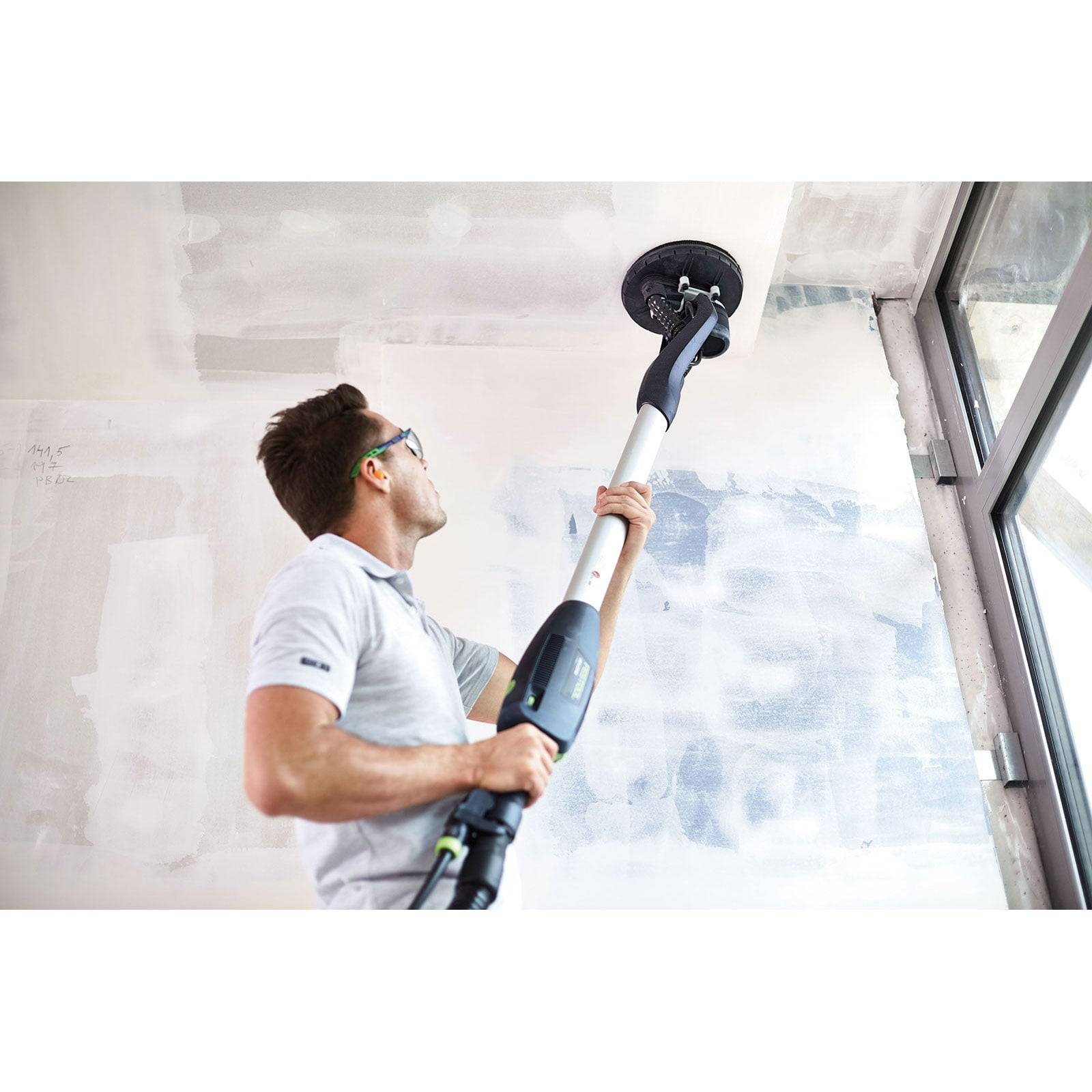 Eine Person benutzt ein Elektrowerkzeug zum Abschleifen einer Decke in einem teilweise fertiggestellten Raum mit weißen und blauen Wänden.