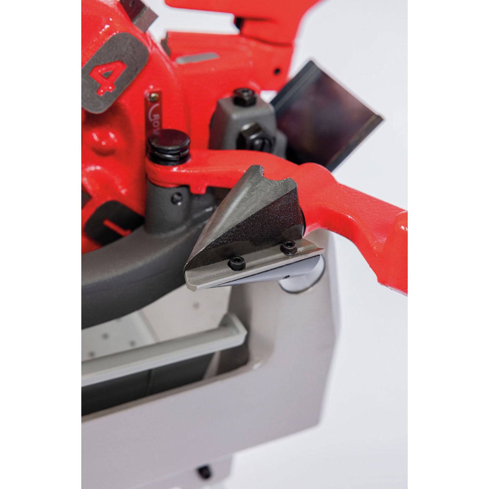 Eine Nahaufnahme eines roten und grauen industriellen Maschinenteils, das eine scharfkantige Metallkomponente und einen schwarzen Gummigriff in einer Fabrikumgebung zeigt.