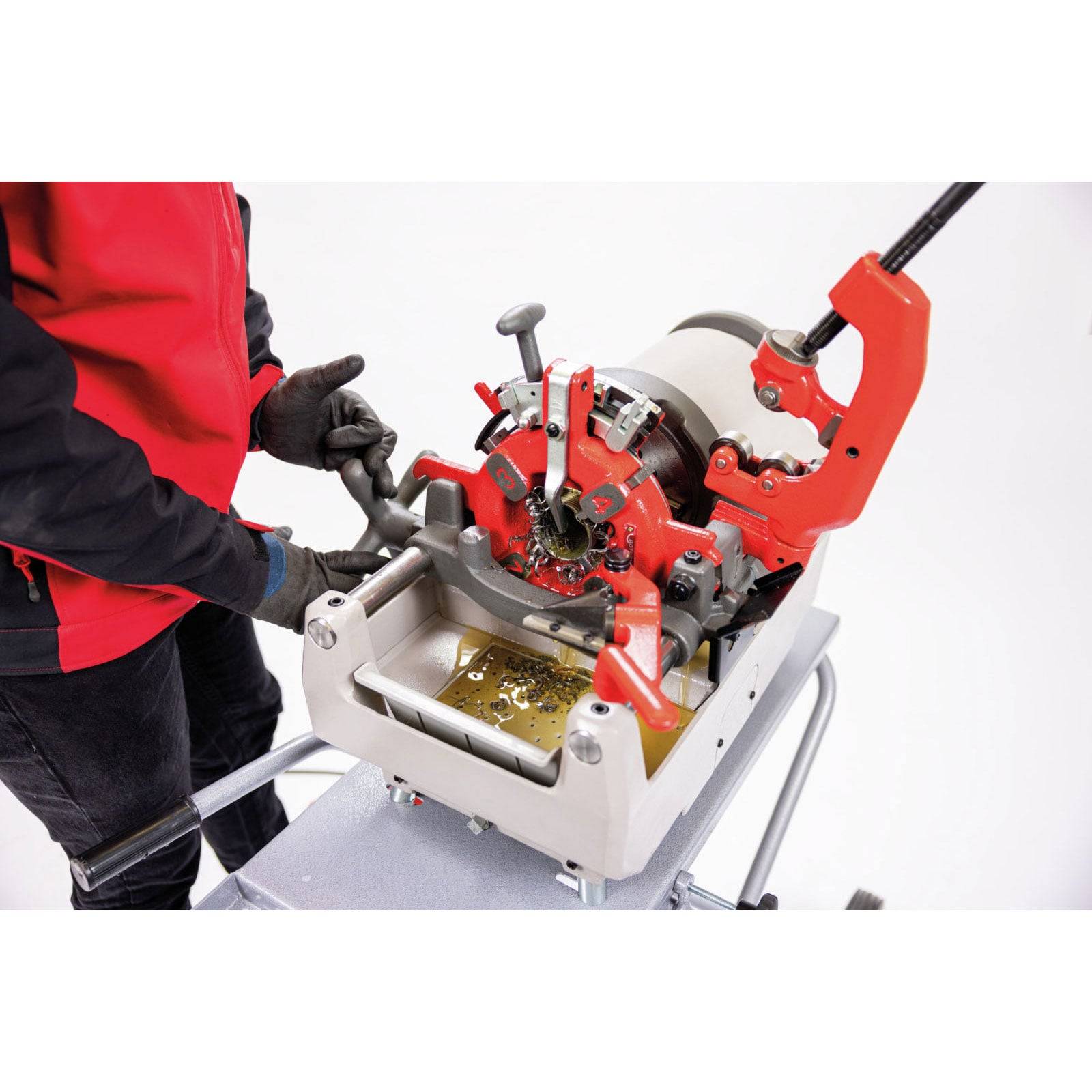 Eine Person in Rot bedient eine Gewindeschneidmaschine für Rohre und führt ein Rohr durch diese. Die Maschine ist auf einem Metallständer montiert.