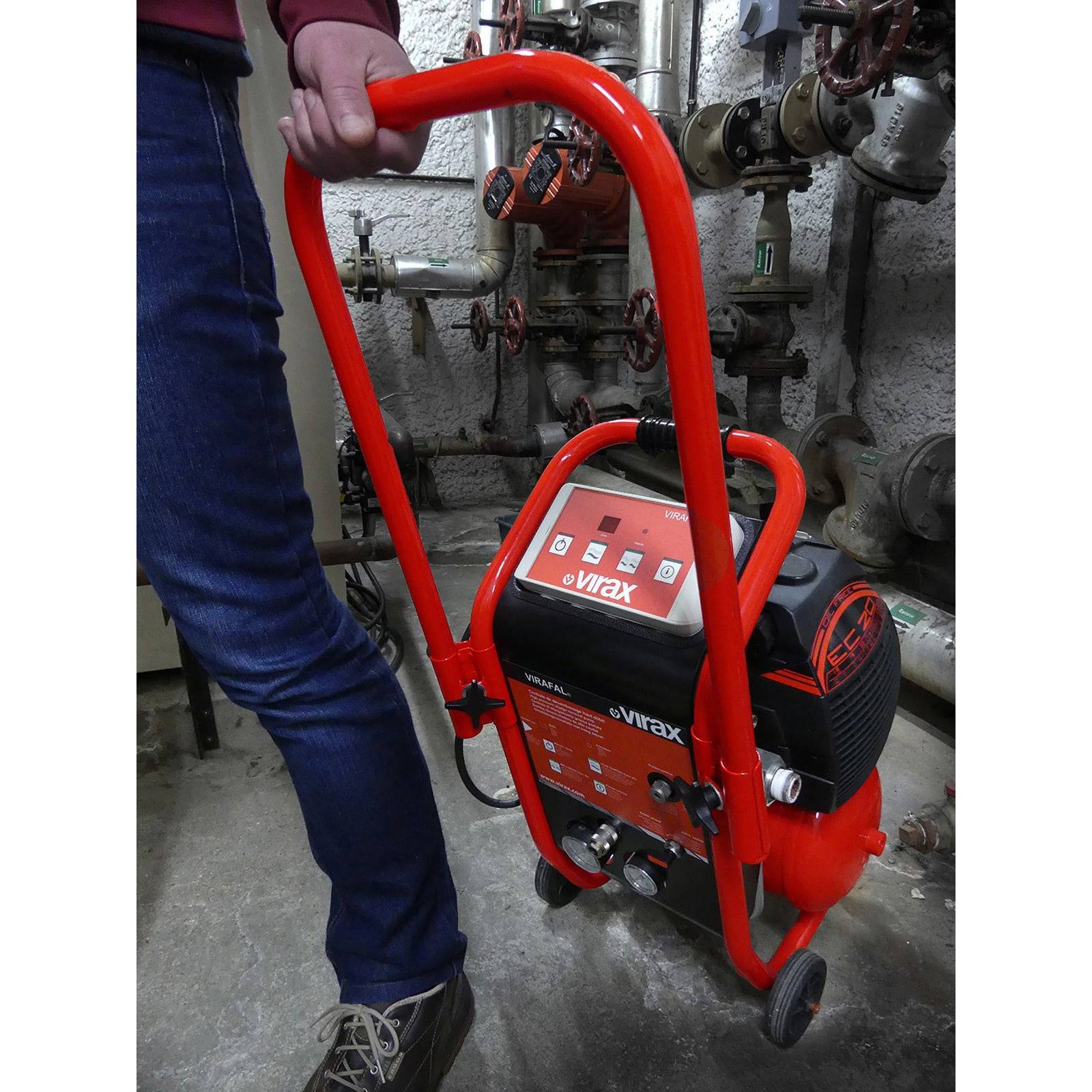 „Eine Person, die einen roten Virax-Hochdruckreiniger in einer industriellen Umgebung mit im Hintergrund sichtbaren Rohren und Ventilen bedient.