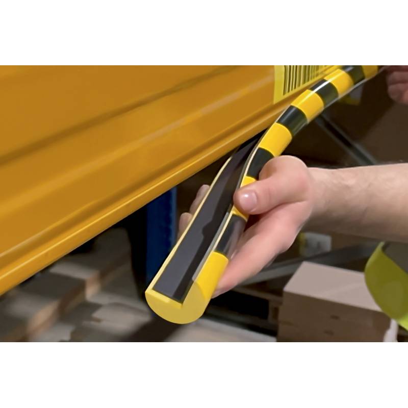 Eine Hand drückt einen gelben und schwarzen Gummipuffer gegen die Kante einer gelben Metalloberfläche, möglicherweise zum Schutz oder zur Sicherheit.