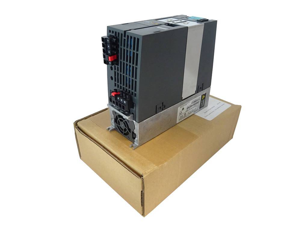 Industrielles Elektronikmodul mit schwarzem Gehäuse mit Lüftungsschlitzen und roten Steckverbindern, das auf einem Versandkarton vor weißem Hintergrund liegt.