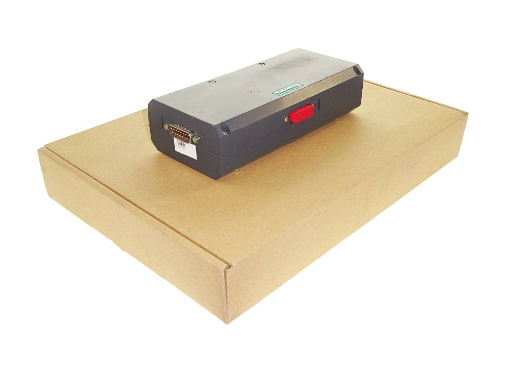 Schwarzes rechteckiges elektronisches Gerät mit einem roten Verschluss liegt auf einem geschlossenen Karton vor einem schlichten weißen Hintergrund.