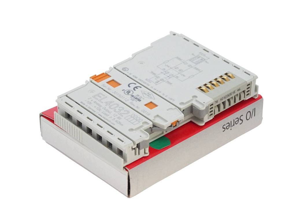 Weisses elektrisches Steuermodul mit Klemmenschlitzen und orangefarbenen Steckverbindern, auf einer rot-weißen Produktverpackung vor einem schlichten Hintergrund.