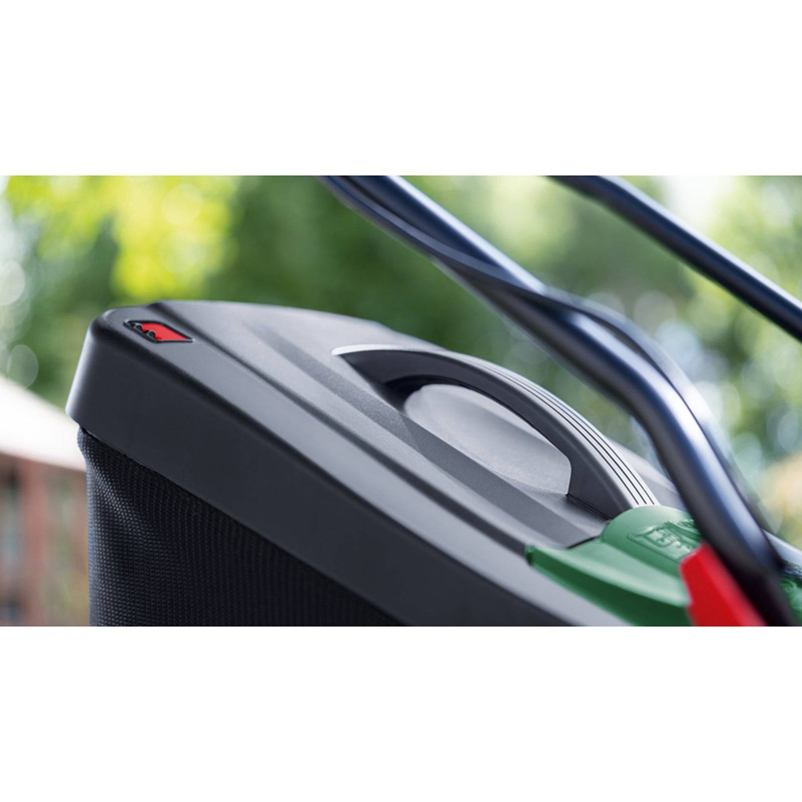 Nahaufnahme eines Rasenmähers-Griffes und Bedienfeldes in einer Gartenumgebung, mit verschwommener grüner Vegetation im Hintergrund.