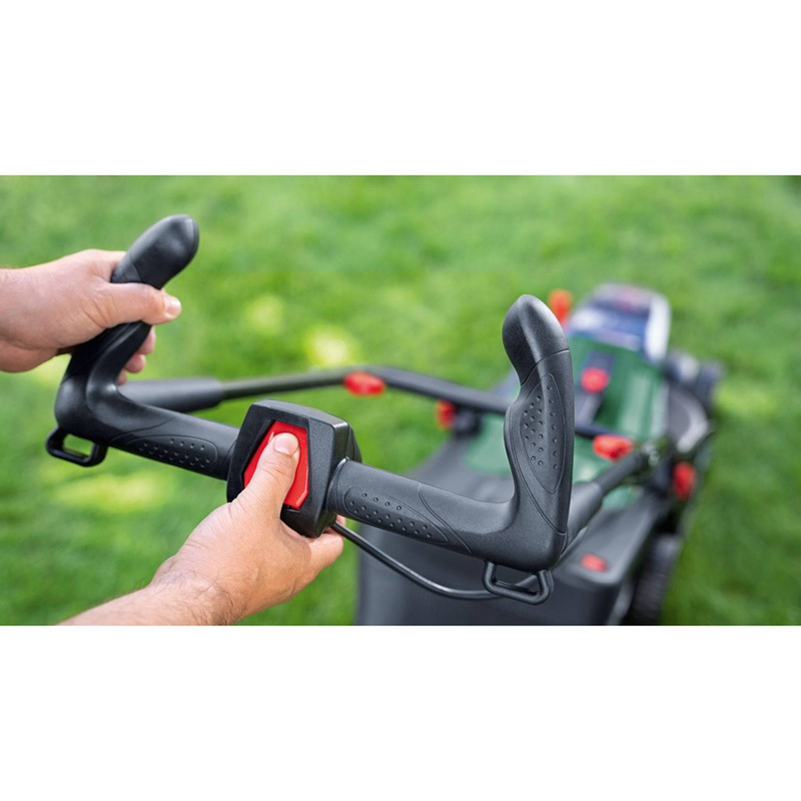 Hände, die den Griff eines Rasenmähers halten, mit Daumen, die einen roten Knopf drücken. Rasenmäher auf einem grünen Rasen, bereit zum Einsatz.