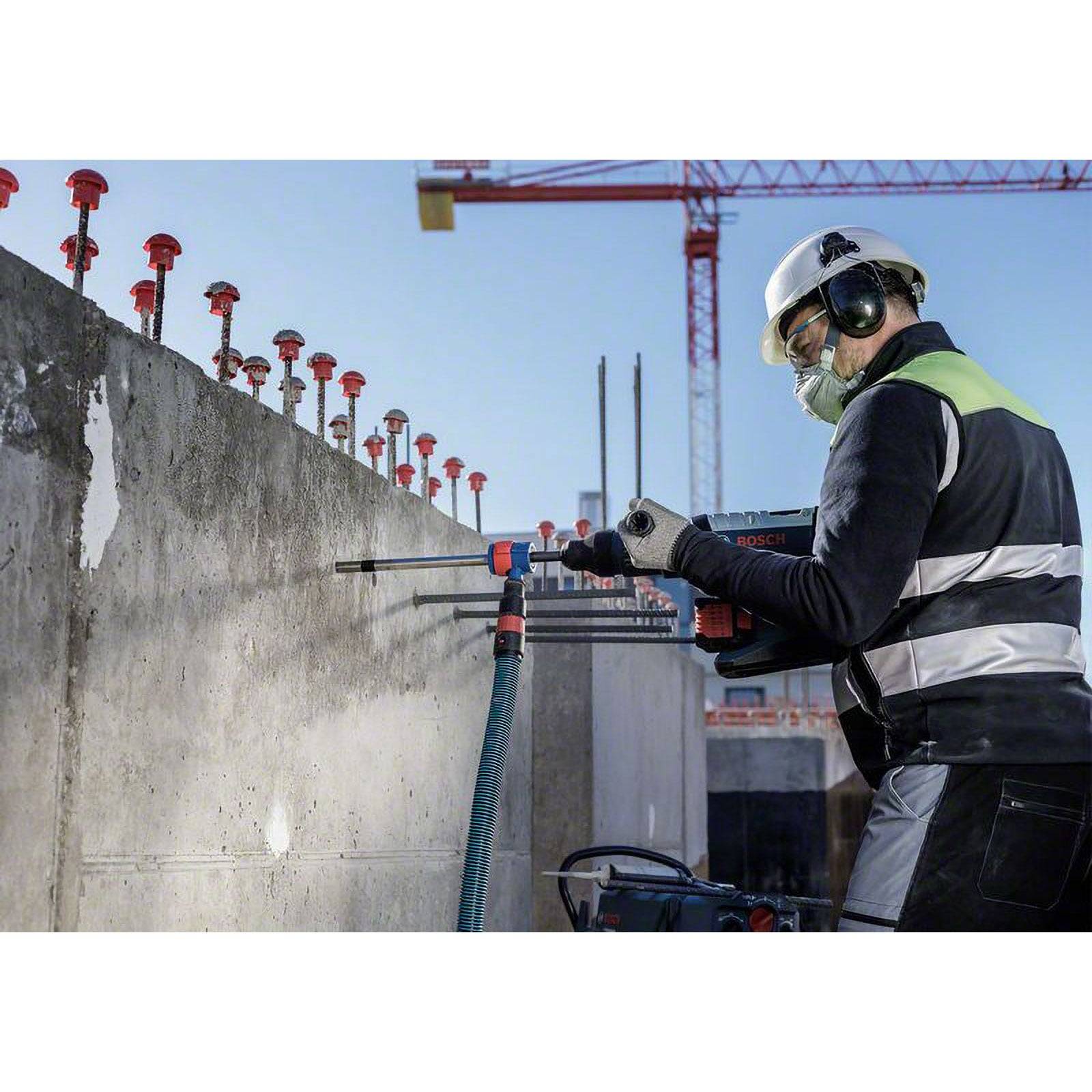 Ein Bauarbeiter verwendet ein Elektrowerkzeug, um eine Betonwand auf einer Baustelle zu bohren, dabei trägt er Sicherheitsausrüstung und einen Helm.