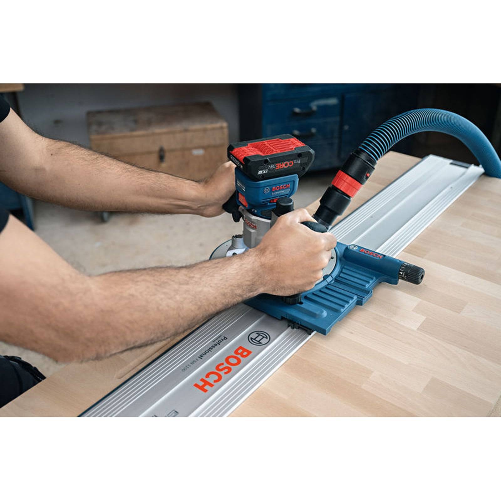 Eine Person verwendet eine Bosch-Oberfräse auf einer Führungsschiene, mit einem Staubsaugerschlauch für die Staubabsaugung. Der Aufbau befindet sich auf einem Holztisch.