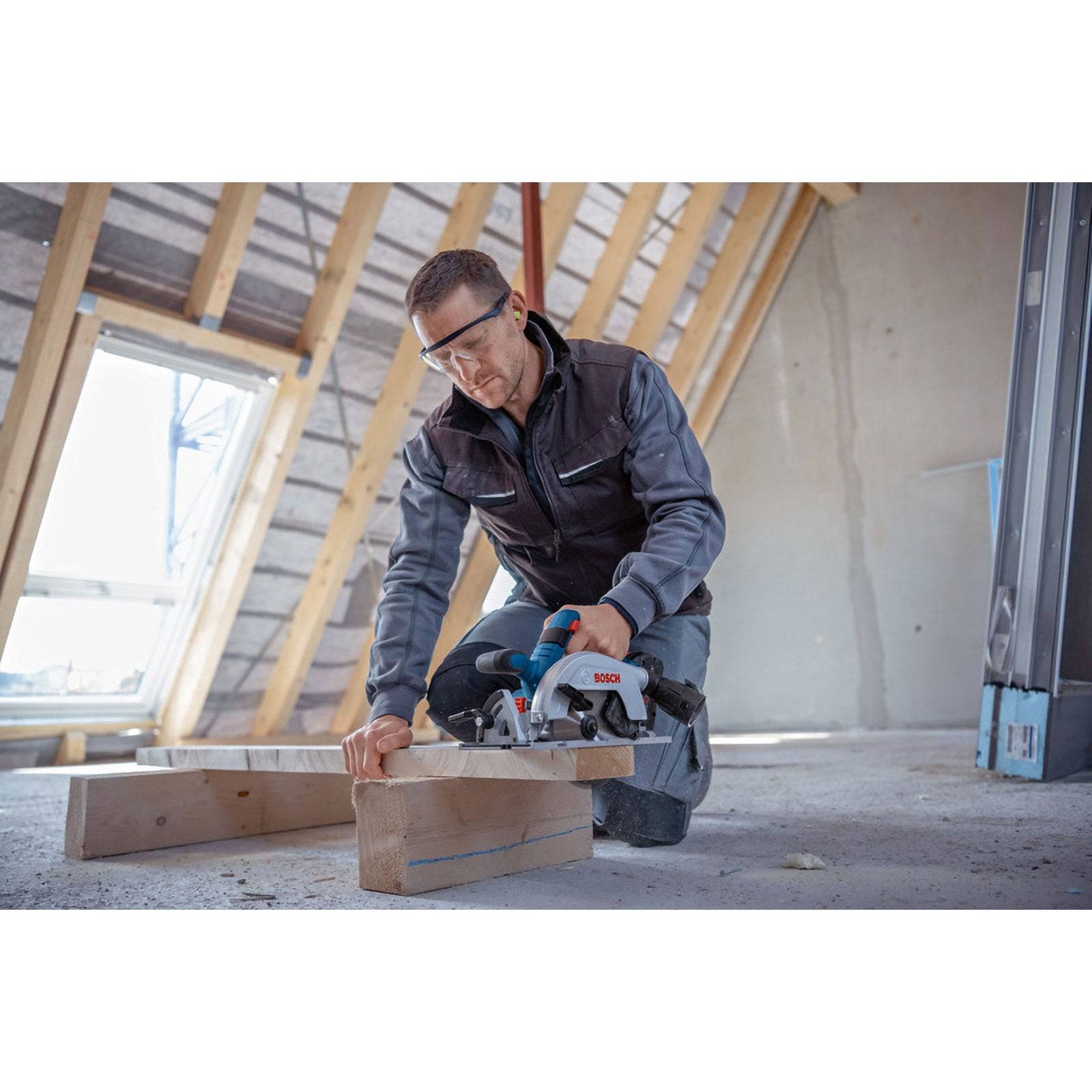 Eine Person in Schutzausrüstung verwendet eine Kreissäge, um Holzbretter in einem teilweise fertiggestellten Gebäude zu schneiden.