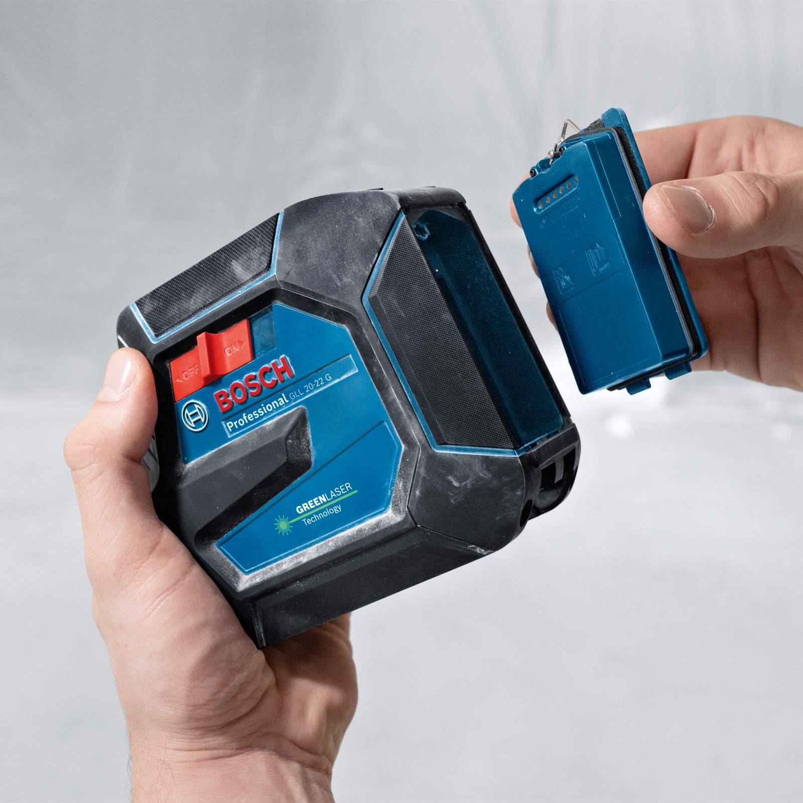 Eine Person hält ein grünes Bosch Professional Laserwerkzeug und zeigt dessen Konnektivität mit einem separaten blauen Gerät.