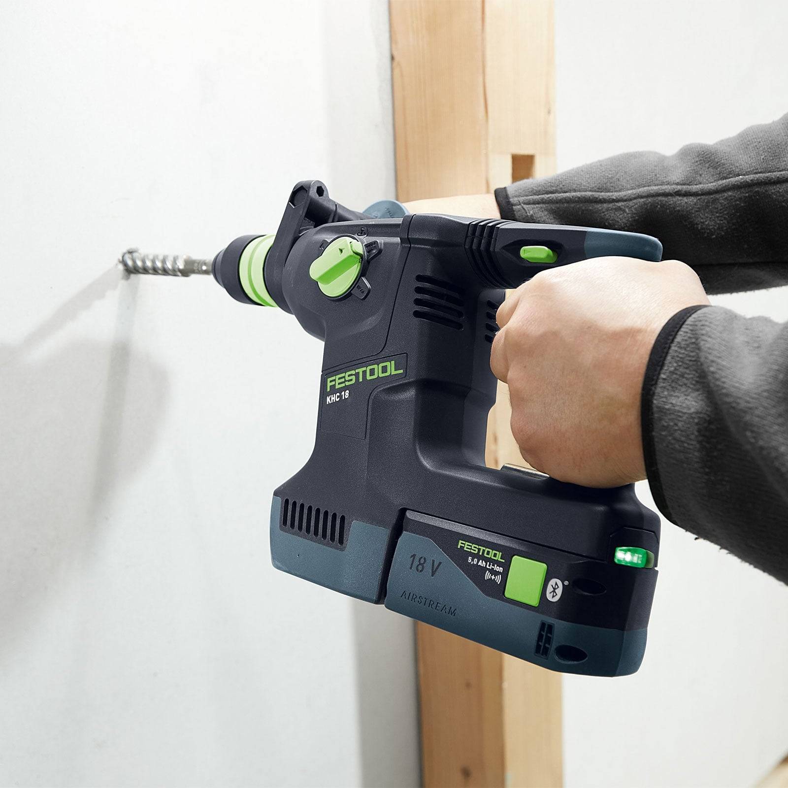 Eine Person, die einen Festool-Akku-Bohrer verwendet, um ein Loch in eine weiße Wand zu bohren und dabei dessen Leistung und ergonomisches Design zur Geltung bringt.
